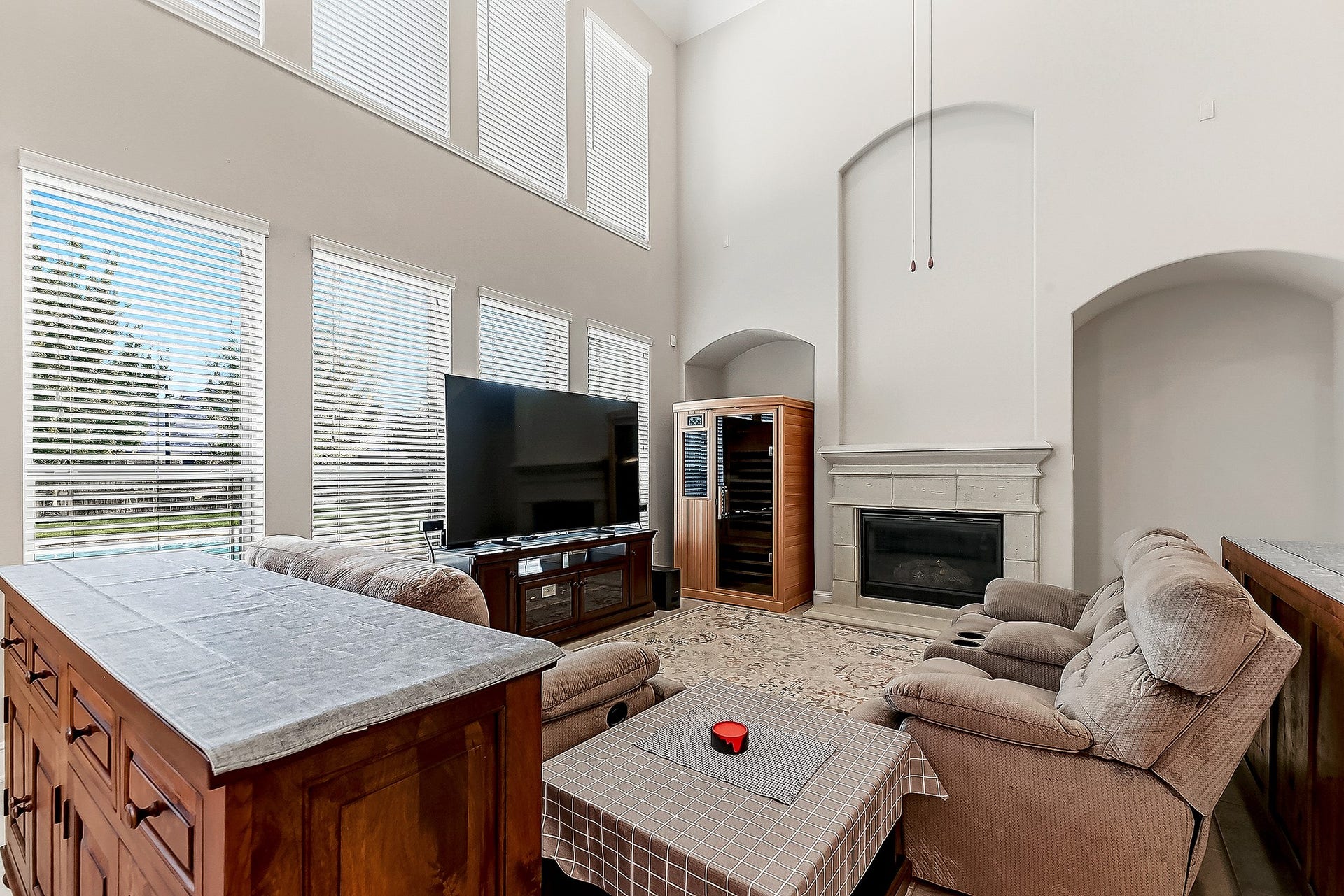 27411 Gladway Manor Drive, Katy, TX 77494 A view of this expansive living room reveals a stunning wall of windows overlooking the backyard, filling the space with natural light. The room features a beautiful stonecast gas fireplace as the focal point, with built-in nooks on either side and a drop-down ceiling fan, adding both style and comfort to this inviting space.
