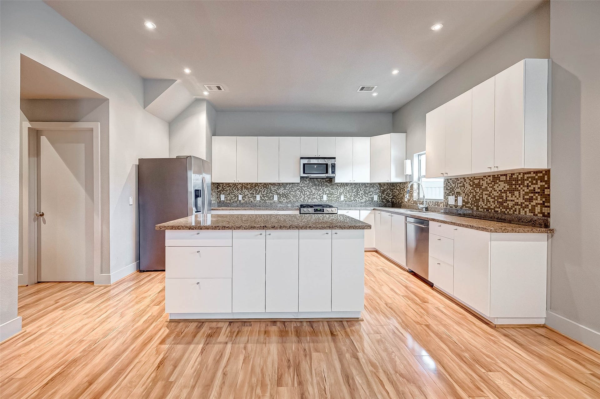 5111 Cornish Street, Houston, TX 77007 Spacious modern kitchen with sleek white cabinetry, granite countertops, and a stylish mosaic backsplash, complemented by stainless steel appliances and warm wood flooring.