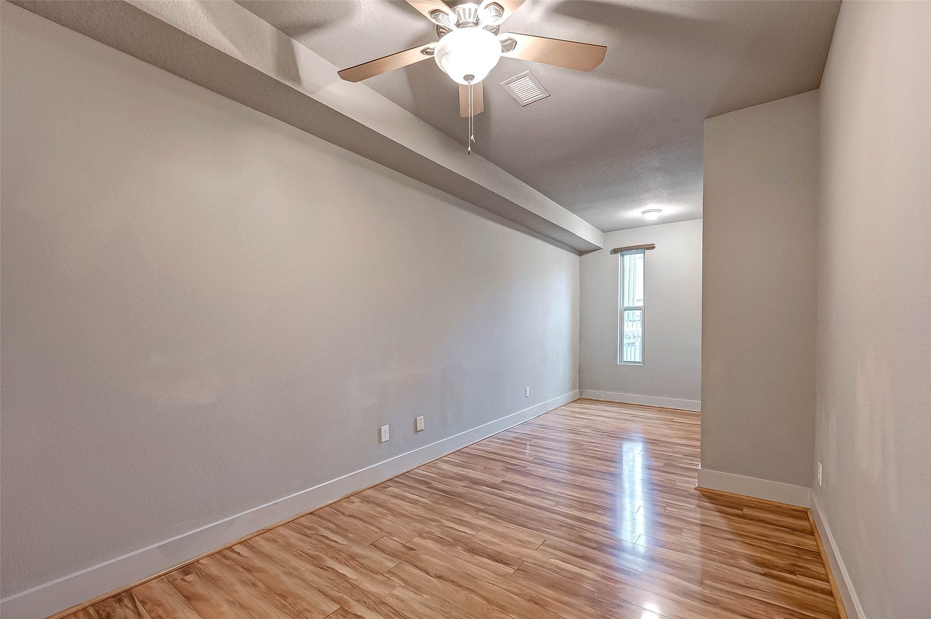 5111 Cornish Street, Houston, TX 77007 Spacious room on FIRST flood with sleek hardwood floors, neutral walls, and a ceiling fan for comfort, accented by natural light from a tall window.