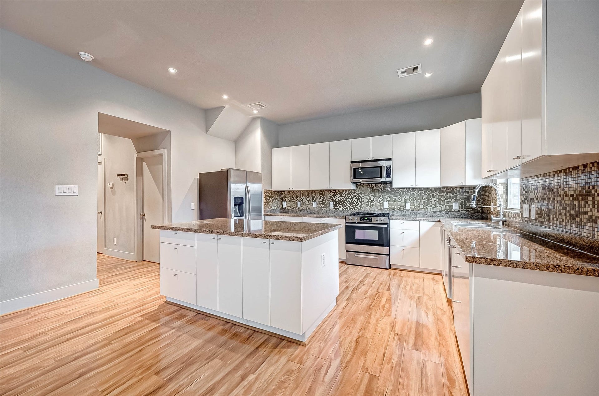 5111 Cornish Street, Houston, TX 77007 Spacious modern kitchen featuring sleek white cabinetry, granite countertops, and stainless steel appliances, complemented by a stylish mosaic tile backsplash and warm wood flooring.