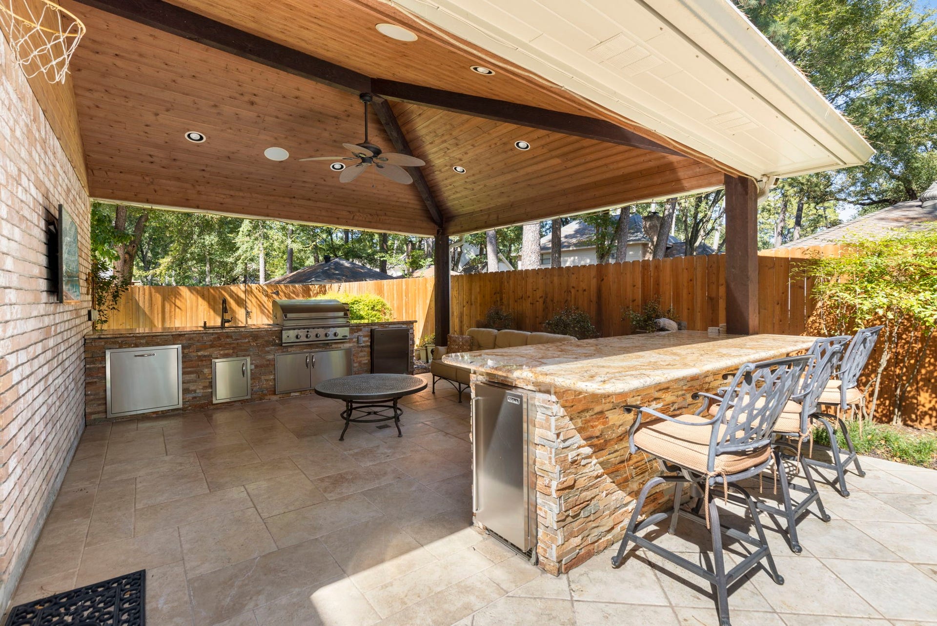 14018 Court Of Regents, Houston, TX 77069 Beneath a wood ceiling, the covered outdoor kitchen features a built in grill, fridge, Perlic ice maker, and generous bar seating for relaxed poolside hosting.