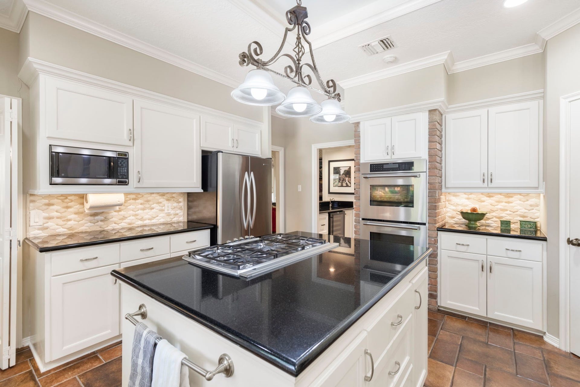 14018 Court Of Regents, Houston, TX 77069 White cabinetry, dark counters, a gas cooktop island, and double wall ovens create a kitchen ready for everyday meals and ambitious entertaining.