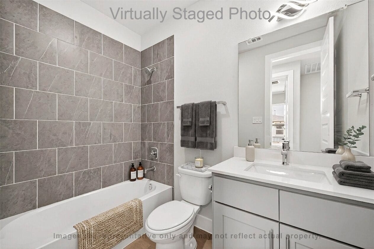 10719 Mason Rd, #32, Richmond, TX 77406 Virtual Staging - Featuring a white bathtub with a grey tile surround, a sleek light grey vanity, and neatly arranged dark grey towels