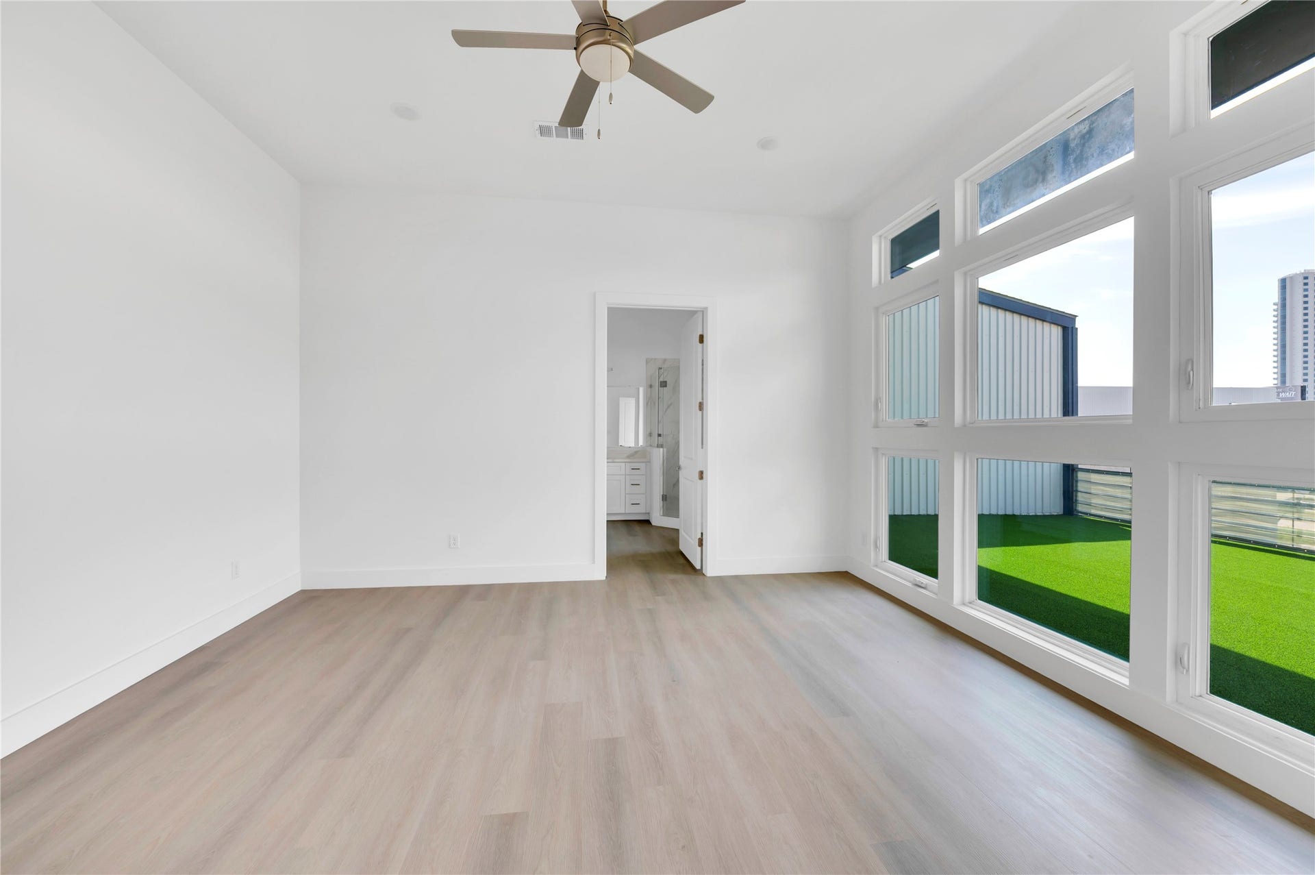 119 Kirby Road, #5303, Taylor Lake Village, TX 77586 Bright and spacious room with sleek hardwood floors, abundant natural light from large windows, and a ceiling fan, leading to an attached bathroom.