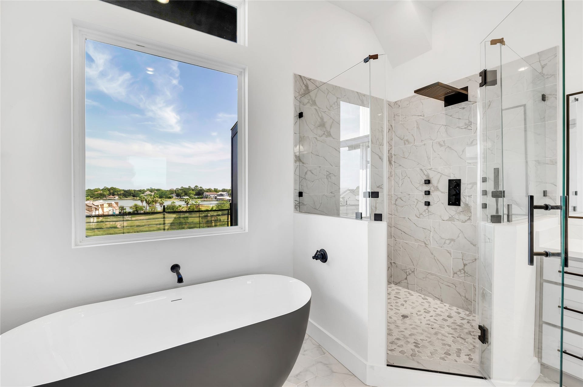 119 Kirby Road, #5303, Taylor Lake Village, TX 77586 Luxurious bathroom featuring a sleek freestanding tub with a stunning view, alongside a spacious glass-enclosed rainfall shower adorned with elegant marble tiles.