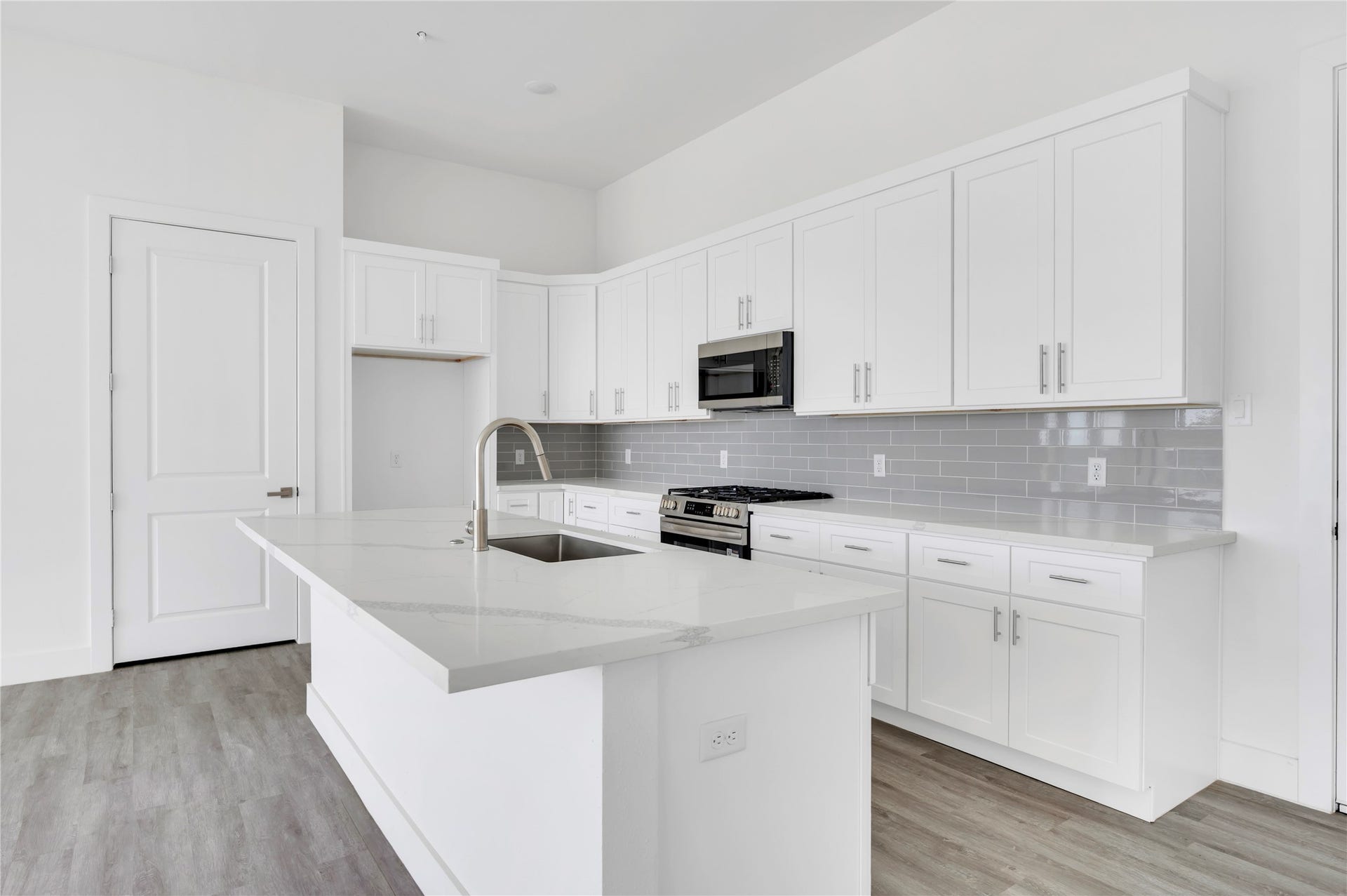 119 Kirby Road, #5303, Taylor Lake Village, TX 77586 Bright and modern kitchen featuring sleek white cabinetry, a spacious island with a built-in sink, and stainless steel appliances, perfectly complemented by a glossy subway tile backsplash.