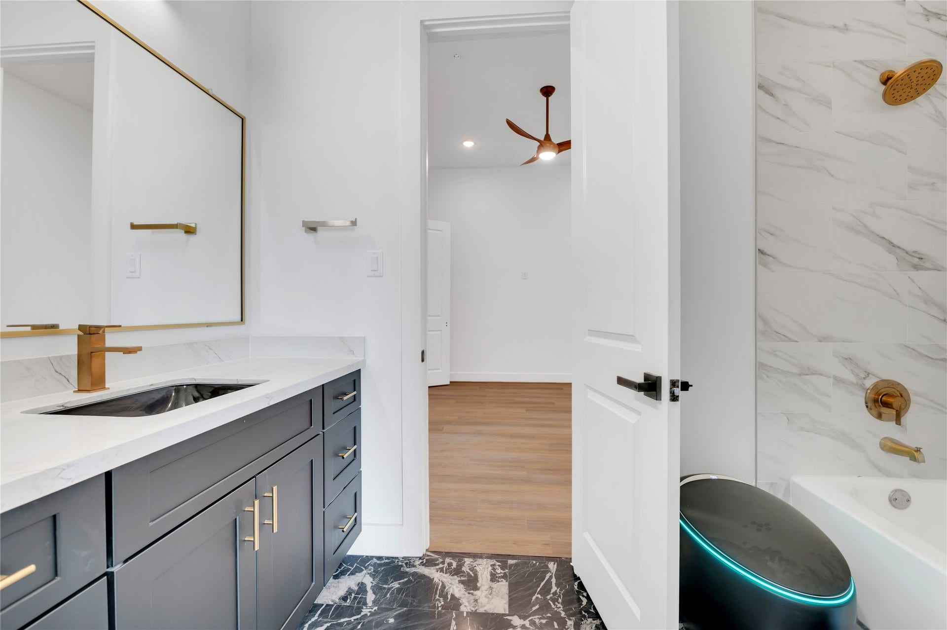 119 Kirby Road, #5303, Taylor Lake Village, TX 77586 Elegant bathroom featuring a sleek vanity with gold fixtures, a luxurious marble-tiled bathtub, and modern black and white accents, leading into a bright room with hardwood flooring.