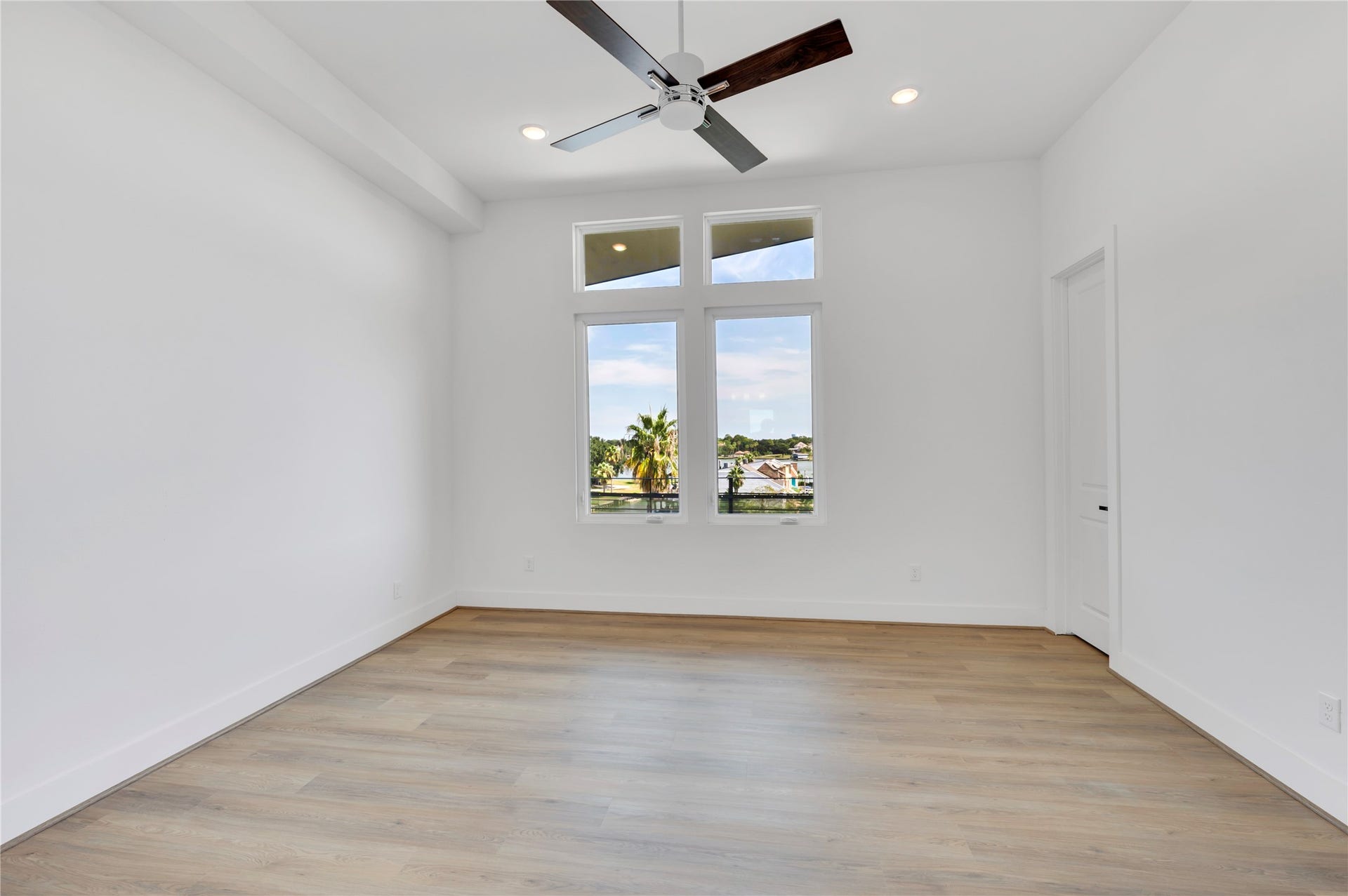 119 Kirby Road, #5303, Taylor Lake Village, TX 77586 Bright and airy room with sleek hardwood floors, high ceilings, and large windows offering scenic views, complemented by a modern ceiling fan.