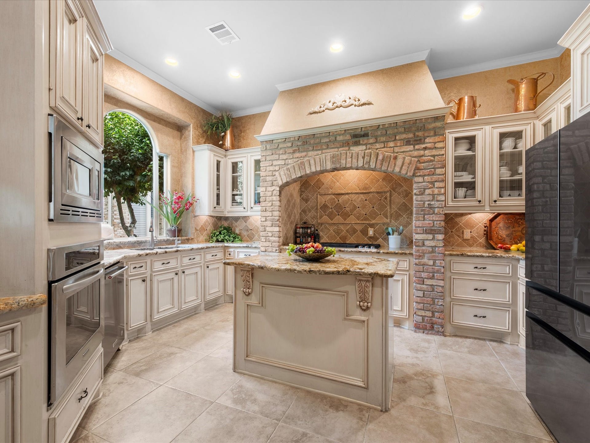 Designed to inspire, the spectacular kitchen showcases expansive cabinetry, abundant storage with dedicated pot and pan drawers, a center island, built-in ovens and microwave, and a striking brick surround framing the recently updated gas cooktop (2024).