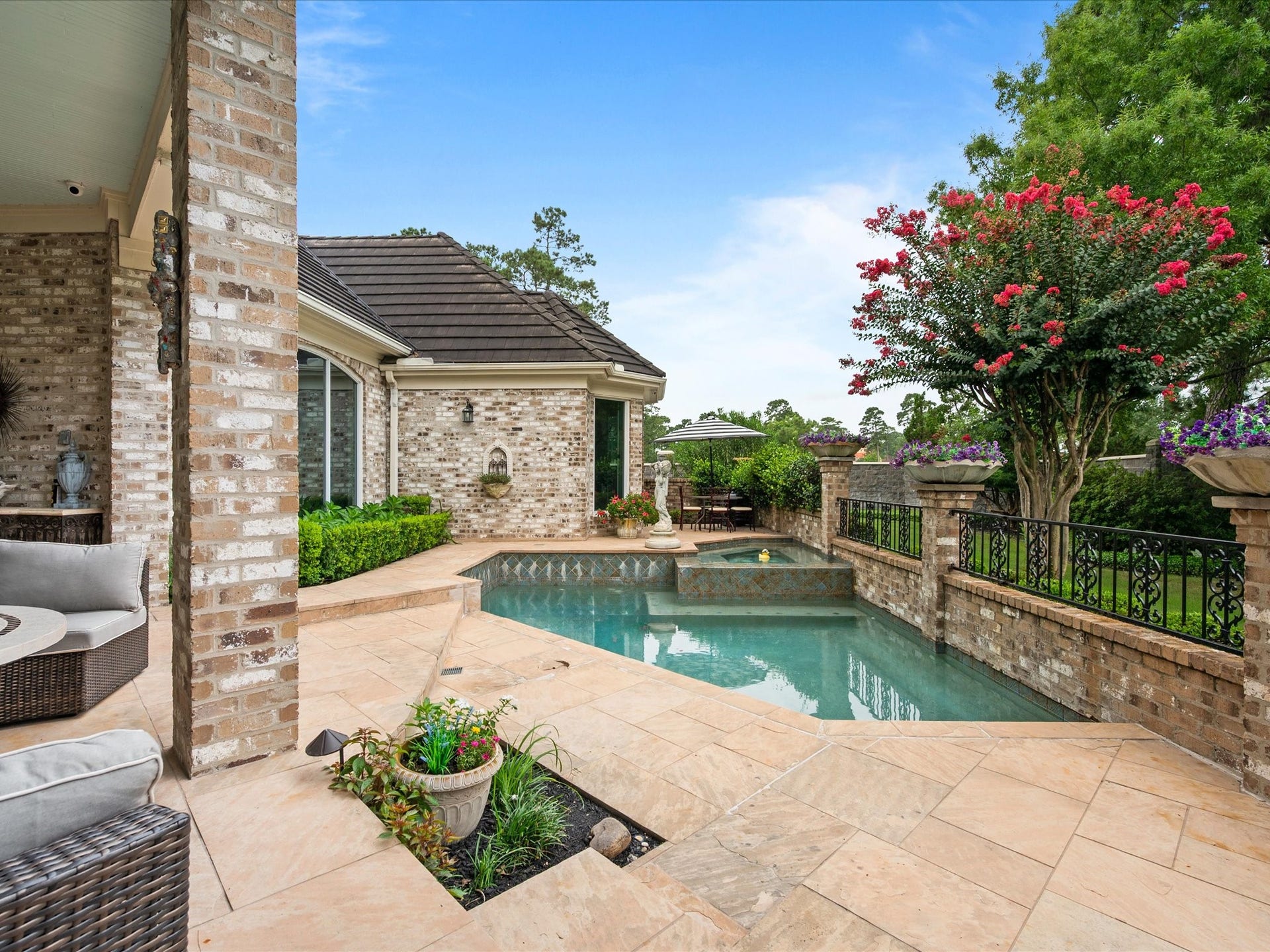 Beautiful landscaping, colorful blooms, and elegant iron fencing surround the pool, enhancing the serene atmosphere of this exceptional outdoor oasis.