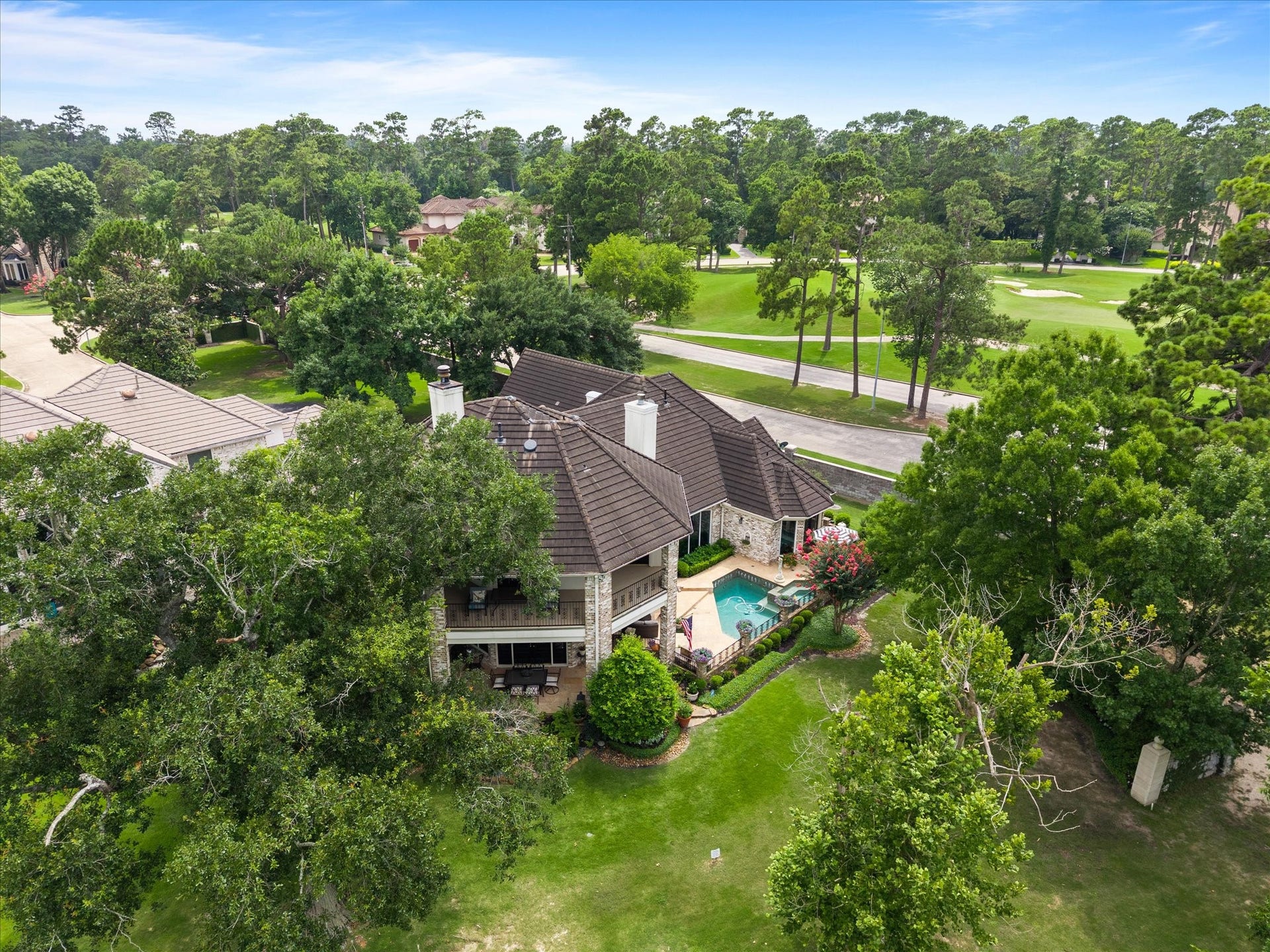 A resort-style outdoor retreat features a sparkling pool, spa, built-in grill, lush gardens, mature trees, expansive patio spaces, and a second-story balcony overlooking the grounds.