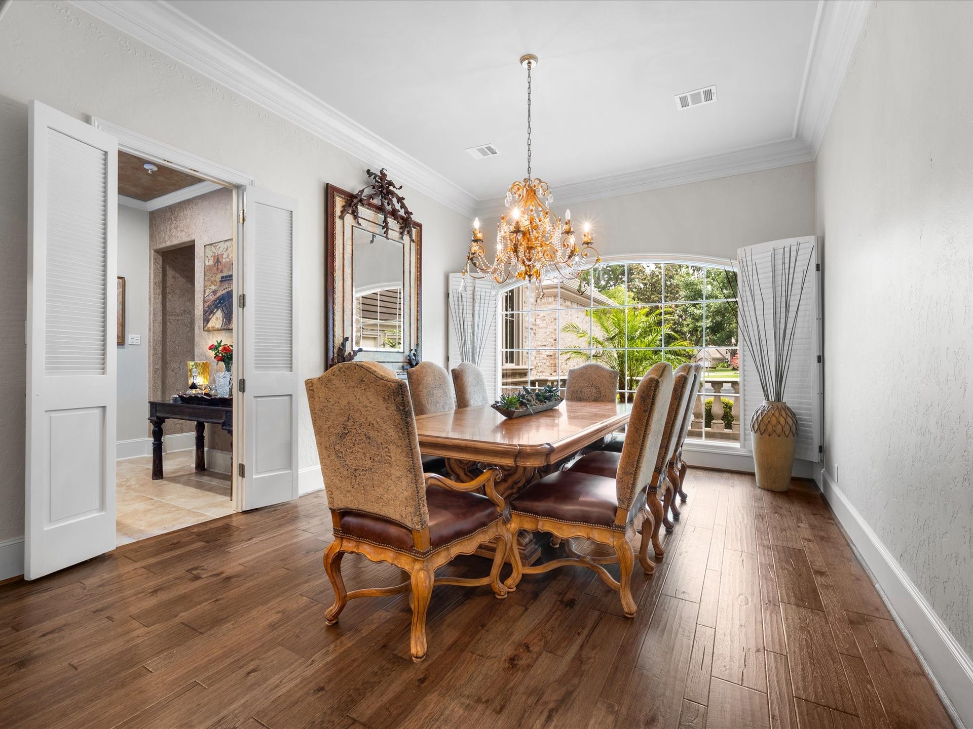 Perfectly positioned just off the wet bar, the formal dining room is framed by expansive windows with shutters, elegant crown molding, and a stunning chandelier, creating an inviting setting for memorable gatherings.