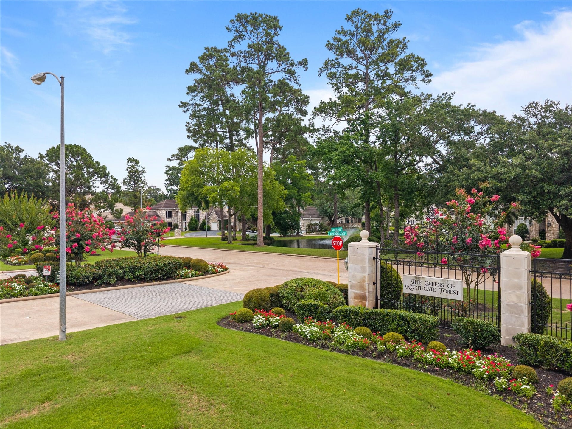 A serene, tree-lined entrance welcomes you into The Greens of Northgate Forest, where lush landscaping, manicured grounds, tranquil pond views, and towering mature trees create an immediate sense of prestige and privacy.