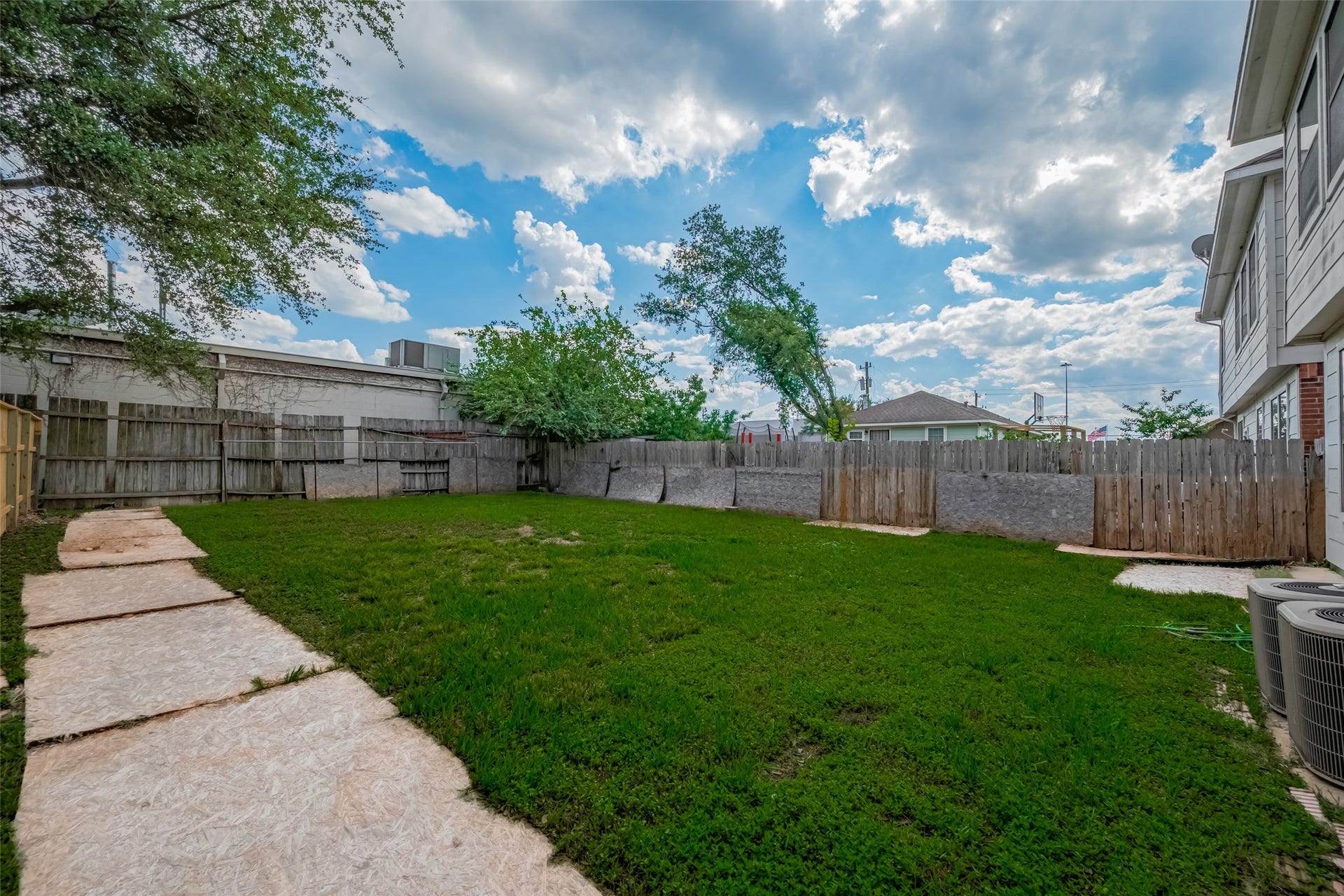 11214 Palmsprings Drive, Houston, TX 77034 View across the backyard shows the lawn, perimeter fencing, and concrete walkway beside the home.