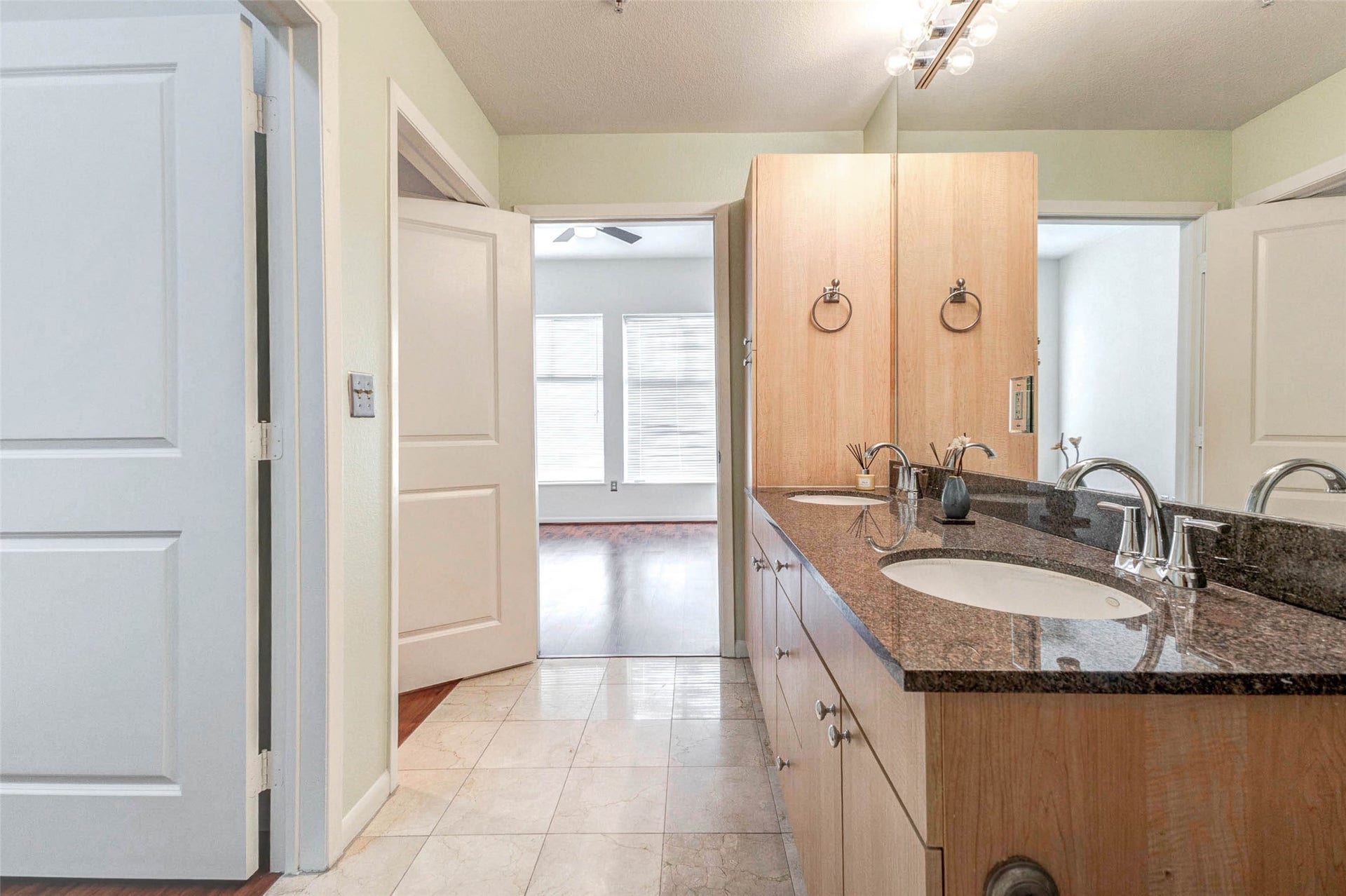 3505 Sage Road, #1104, Houston, TX 77056 From the bathroom, you can see the convenient connection to the primary bedroom, creating a comfortable suite-style layout. The long granite vanity offers plenty of counter space while the warm wood cabinetry provides storage for everyday essentials. The open doorway leads directly back into the bedroom, allowing natural light to flow between the spaces. This thoughtful layout enhances both functionality and privacy within the home.
