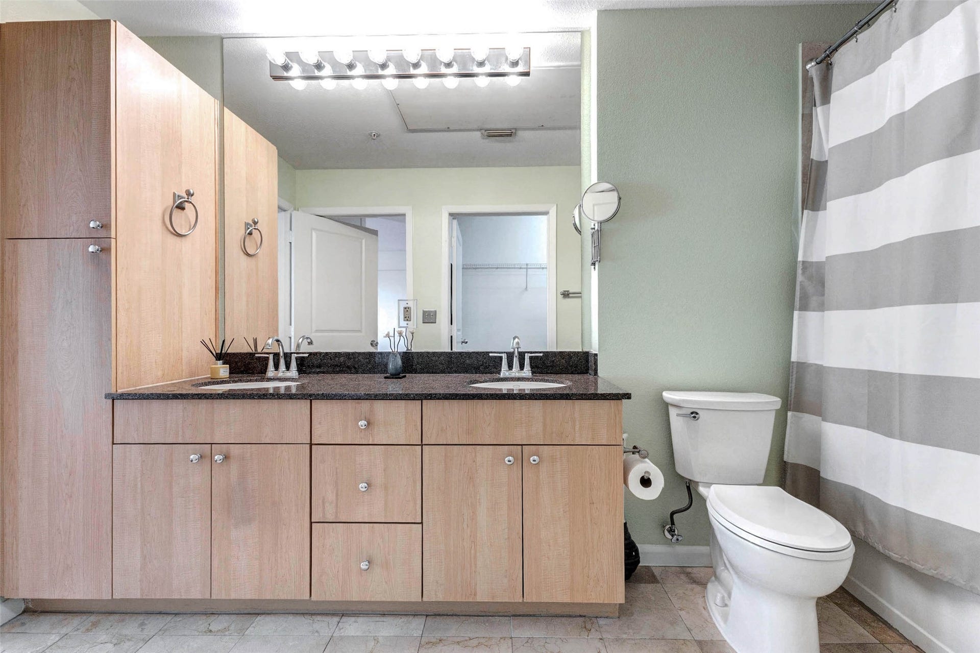 3505 Sage Road, #1104, Houston, TX 77056 This view showcases the full bathroom layout, featuring the long granite vanity, generous cabinet storage, and a well-positioned tub and shower combination. Neutral tile flooring and soft wall tones create a calm and welcoming atmosphere. The oversized mirror and bright vanity lighting provide excellent illumination while visually expanding the space. Designed for both comfort and efficiency, the bathroom offers plenty of room for daily routines while maintaining a clean, contemporary style.