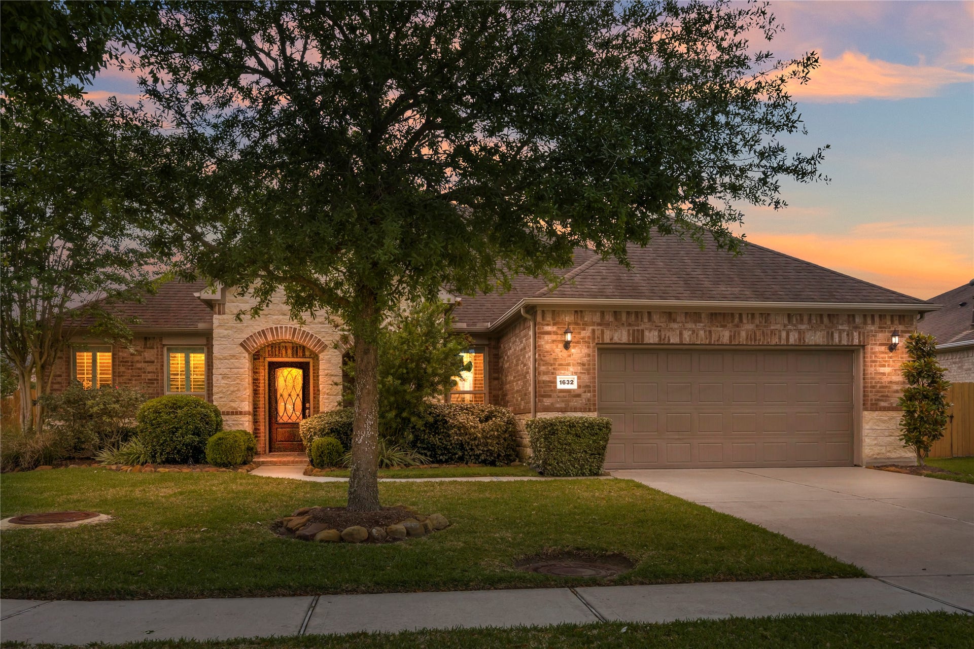 This charming single-story home features a brick exterior with a three-car tandem garage and a welcoming front entrance. The well-maintained front yard includes a mature tree and shrubbery, creating a cozy and inviting curb appeal.