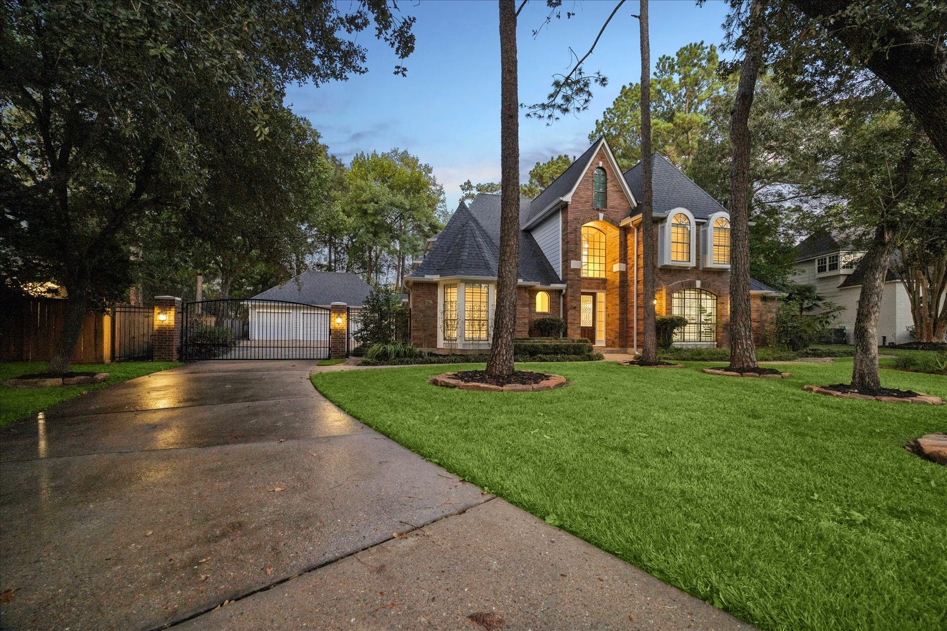 Evening exterior showcasing the motorized driveway gate and distinguished arrival. 3 finished car garage with epoxy floors.