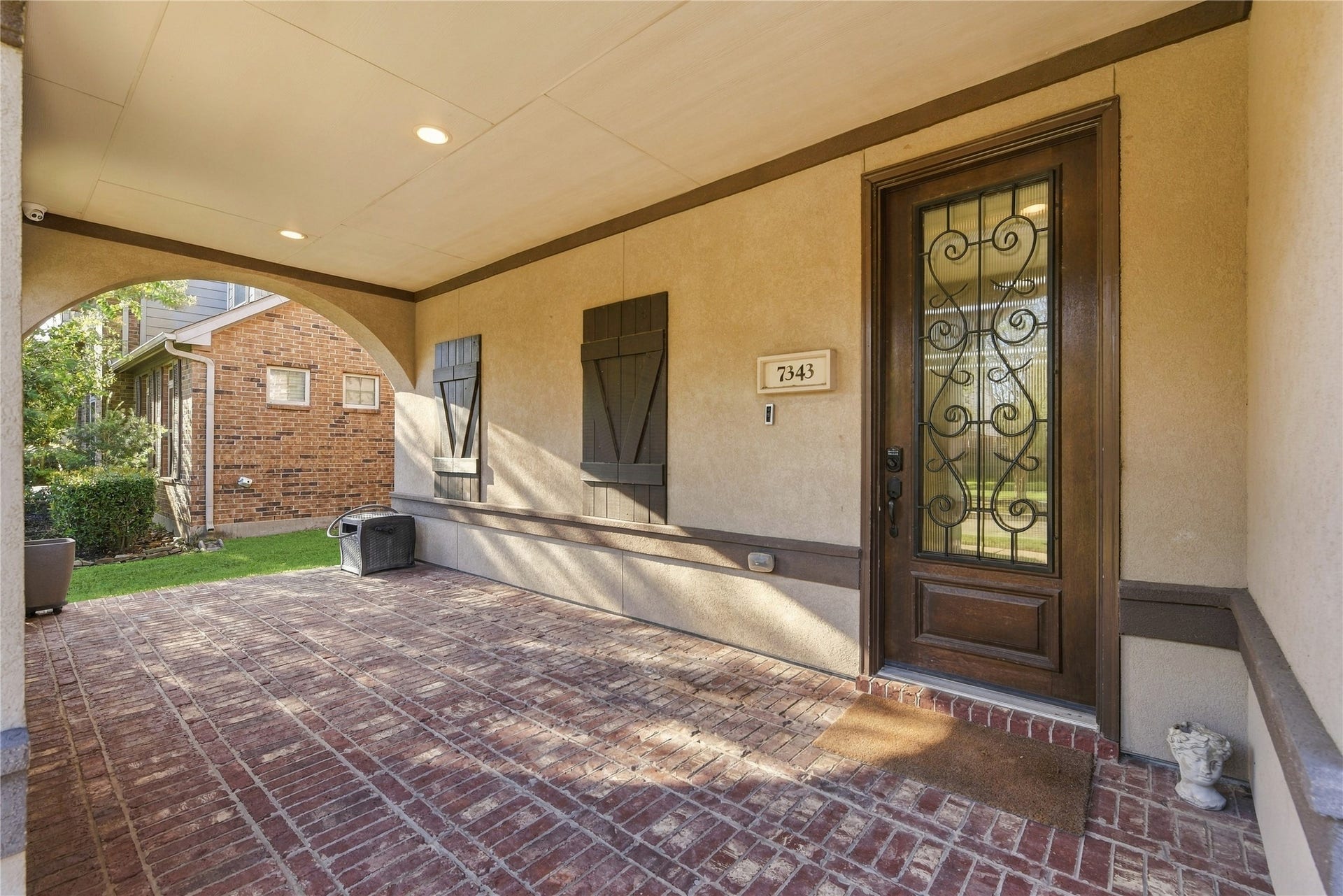 7343 Meadowcroft Boulevard, Sugar Land, TX 77479 An inviting covered entryway with wrought iron door and classic brick flooring, offering a warm welcome to your new home.