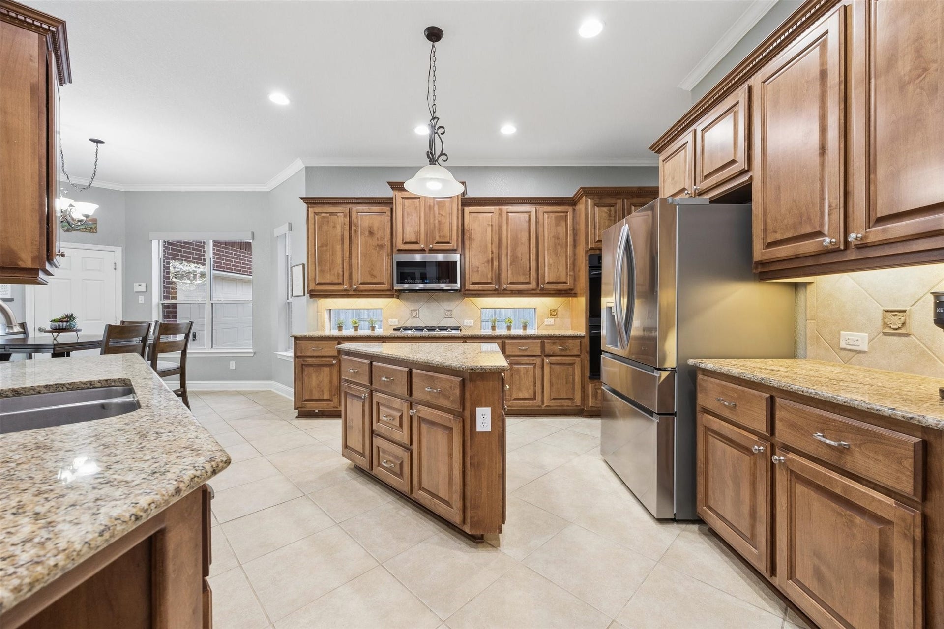 3523 Silvercreek Drive, Manvel, TX 77578 Kitchen with tile flooring, island, built-in wood cabinetry, granite countertops with tile backsplash open to breafast area