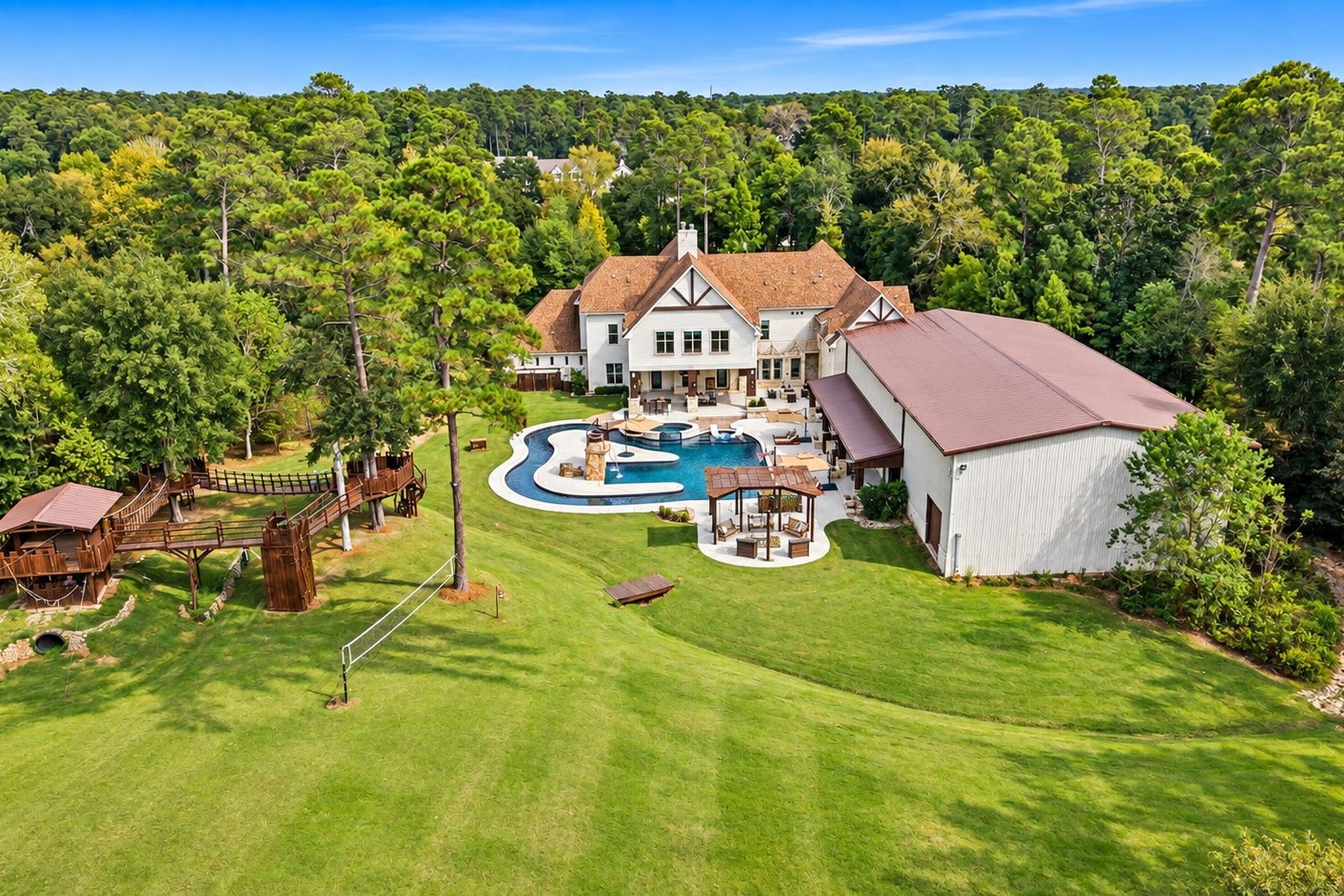 37753 Marias Way, Magnolia, TX 77354 An aerial view showcases the scale of the estate, with the residence, resort-style pool and lazy river, expansive lawn, metal building and elaborate treehouse tucked among the trees.