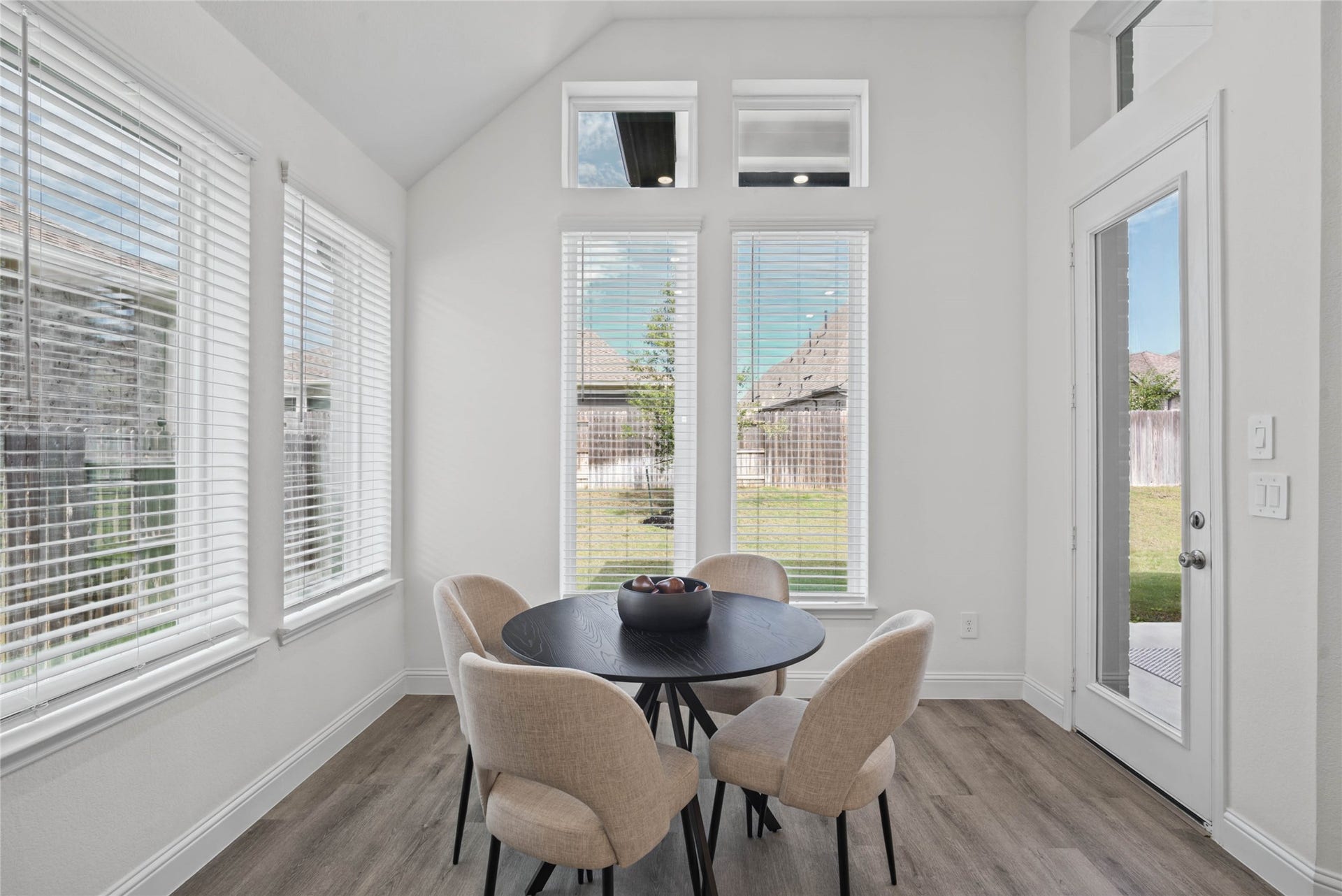 The breakfast area is filled with natural light and features high ceilings, recessed lighting, expansive windows with fitted blinds, and an access door to the back covered patio.