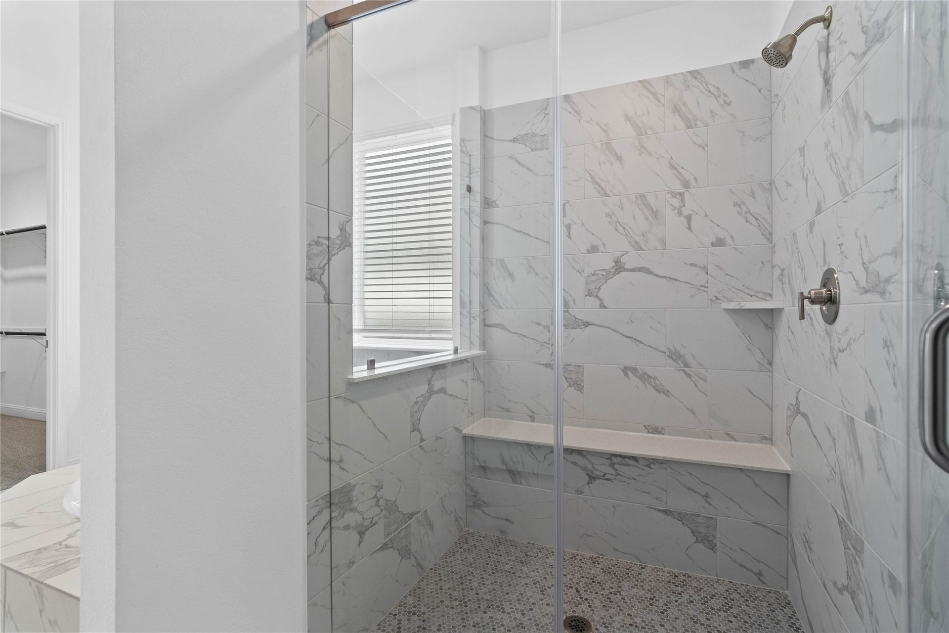 The walk-in shower includes a convenient, integrated bench with a niche shelf, offering comfort, extra storage space, and a high-end, custom appearance.