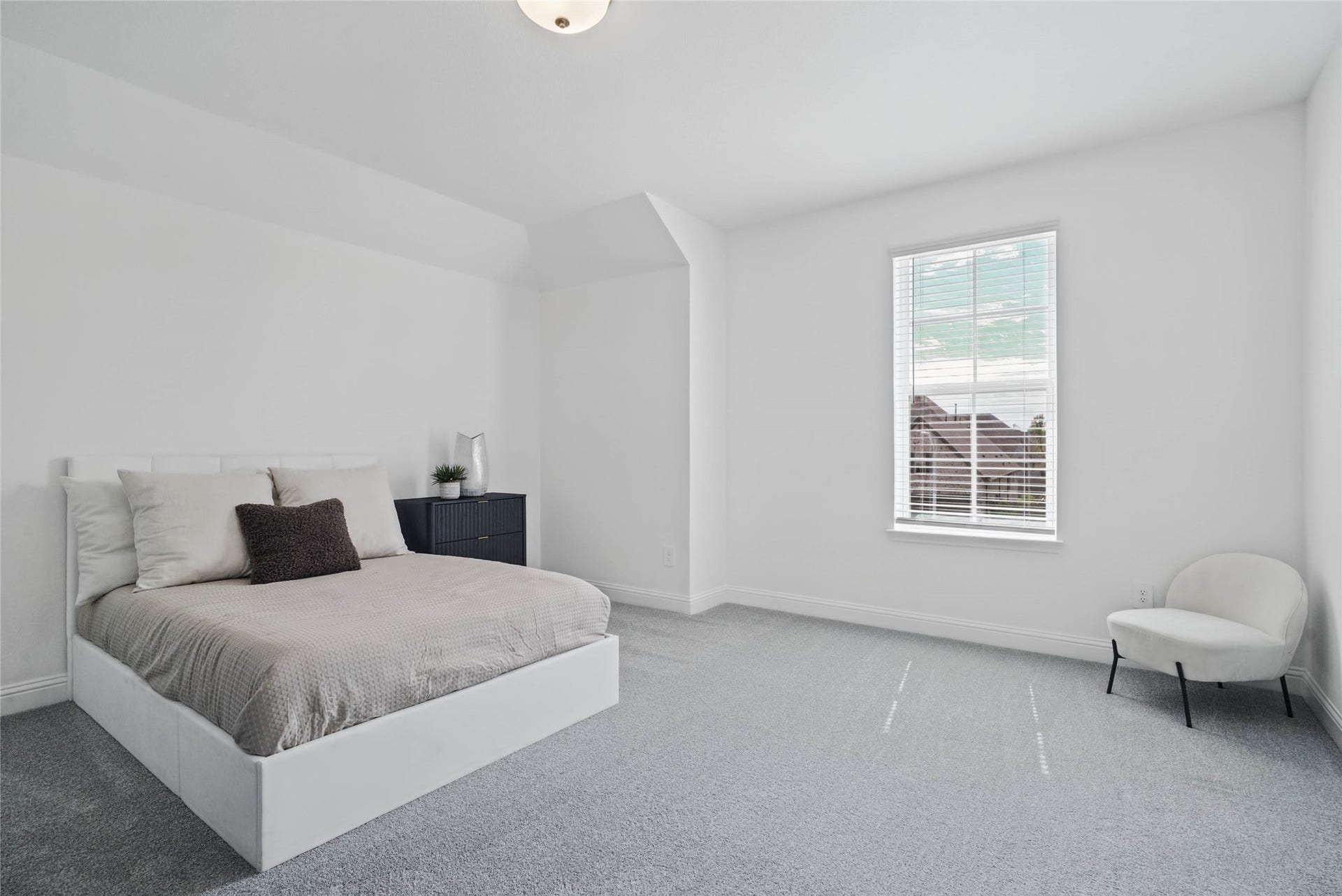 Spacious secondary bedroom features high ceilings, neutral tone walls, plush carpet flooring, and a large window fitted with blinds.