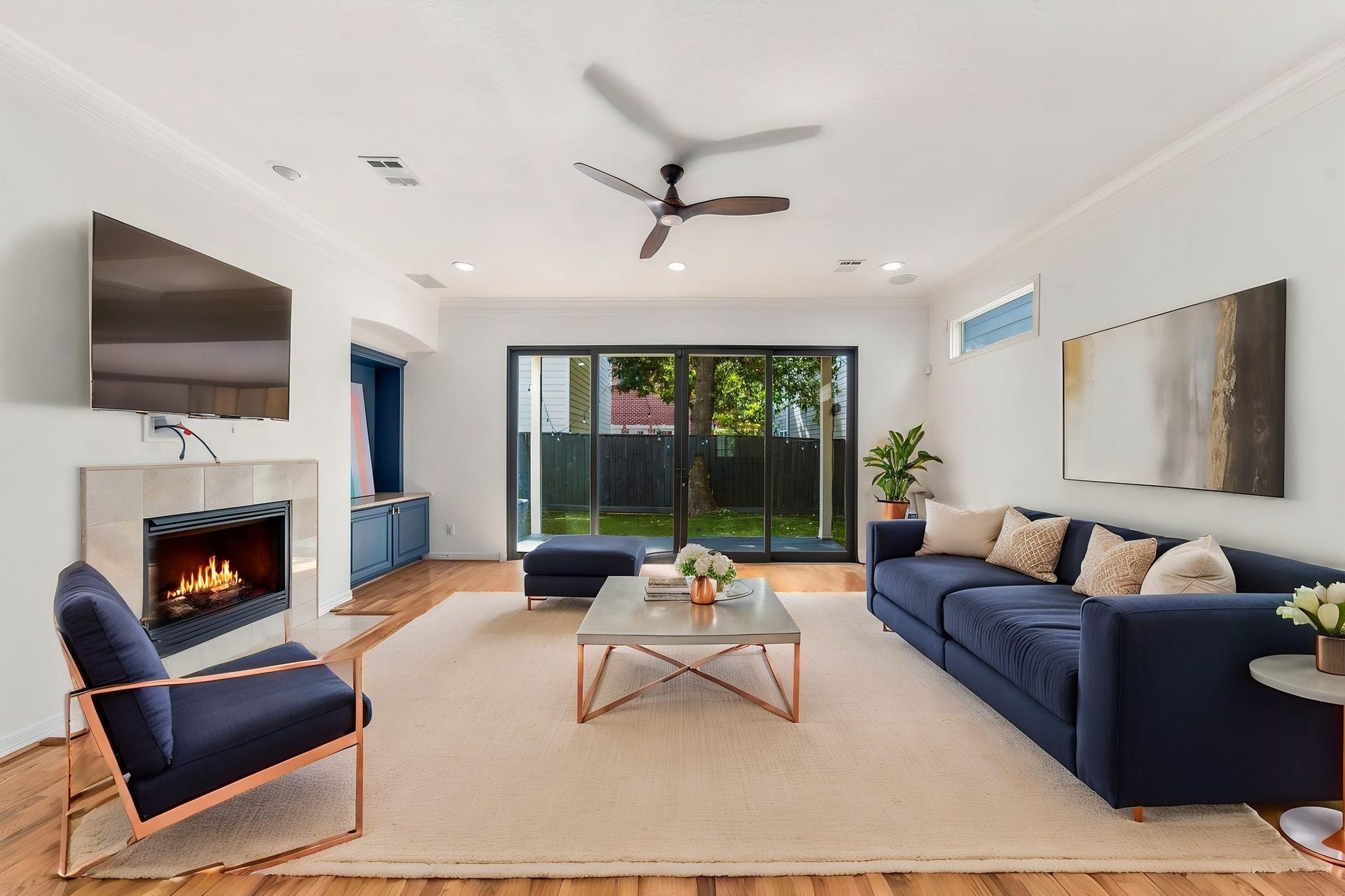 6113 Maxie Street, Houston, TX 77007 A spacious, light-filled living room featuring hardwood floors, fireplace, crown molding & built-in surround sound. Expansive sliding glass doors overlook the private backyard, creating a seamless connection between indoor & outdoor living. Virtually staged.