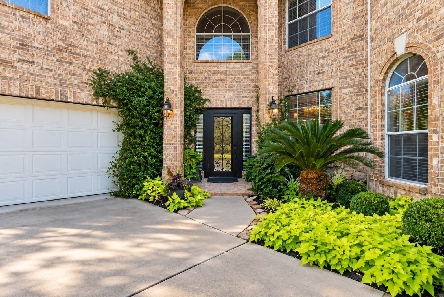 25734 Jewel Springs Lane, Katy, TX 77494 A dramatic two-story recessed entry, framed by lush landscaping and an ornate iron-and-glass door, offers a glimpse of the elegance within.