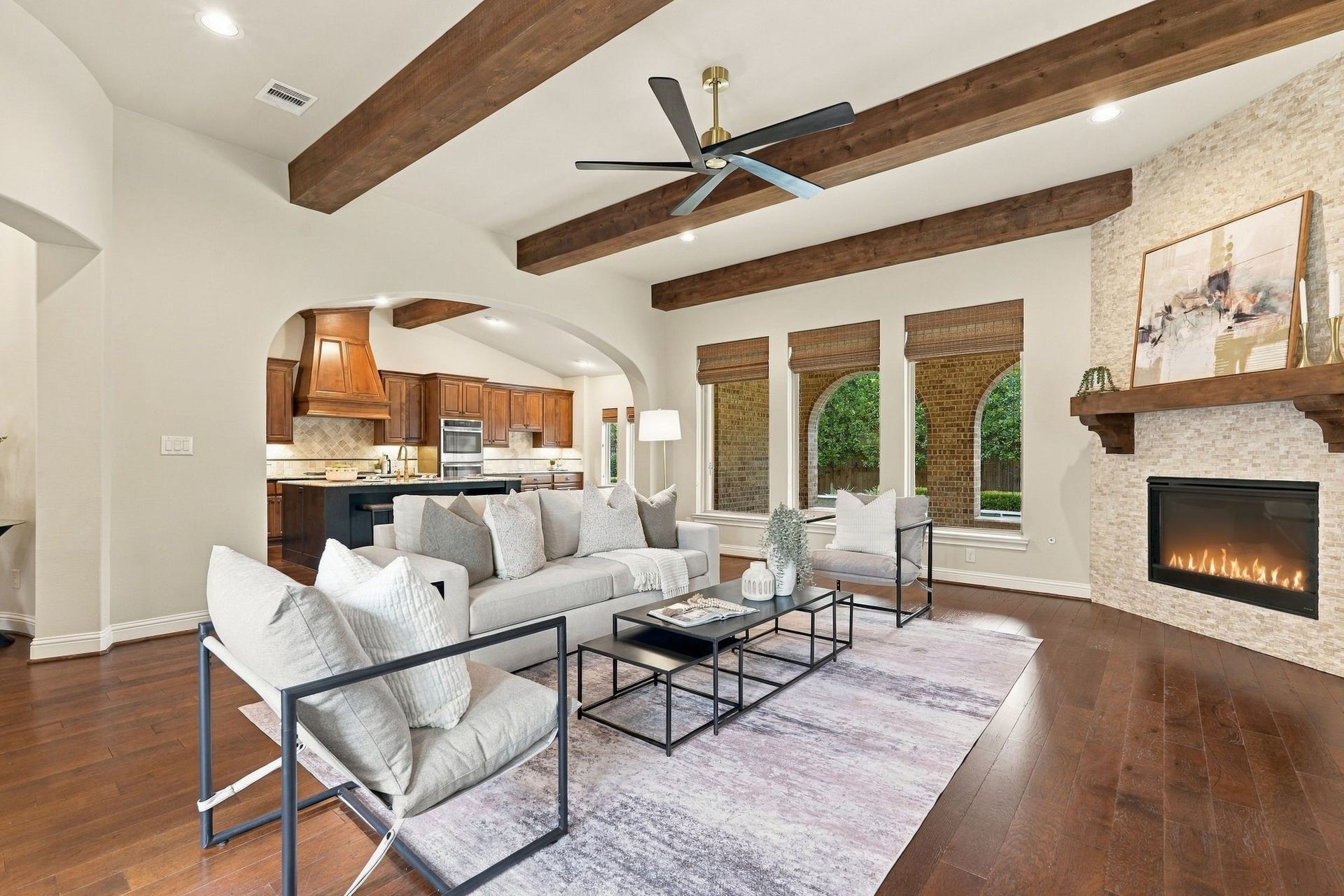 51 Woodglade Way, The Woodlands, TX 77375 Warm and inviting living space with rich hardwood floors, dramatic exposed beams, a floor-to-ceiling stone fireplace, and architectural arches that complement the homes Mediterranean-inspired design. Expansive windows overlook the pool and the courtyard.