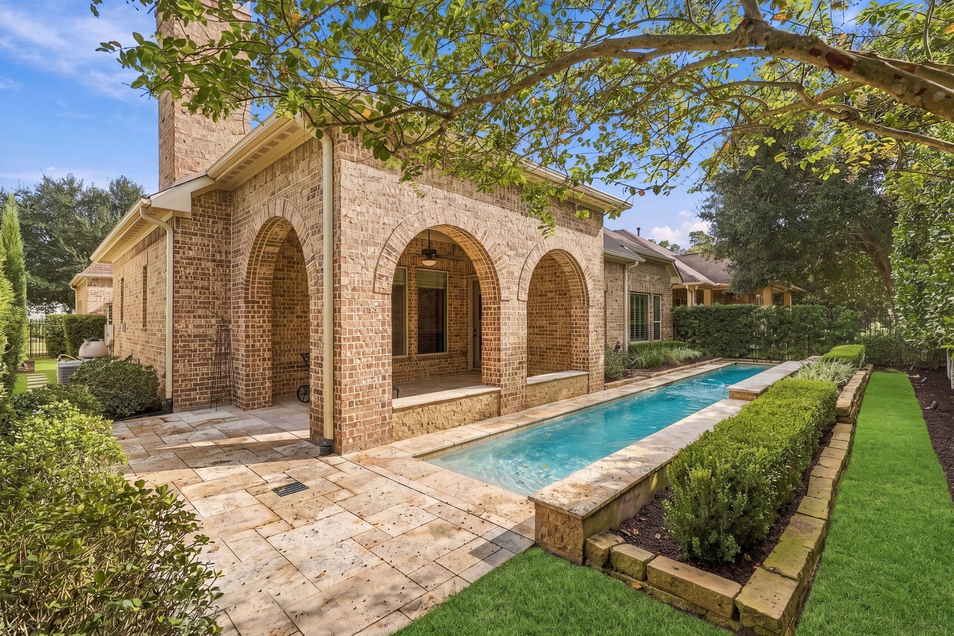 51 Woodglade Way, The Woodlands, TX 77375 A private resort-style lap pool is framed by lush landscaping, mature trees, and elegant stone decking. Covered outdoor living with graceful brick arches creates a peaceful setting for relaxing or entertaining.