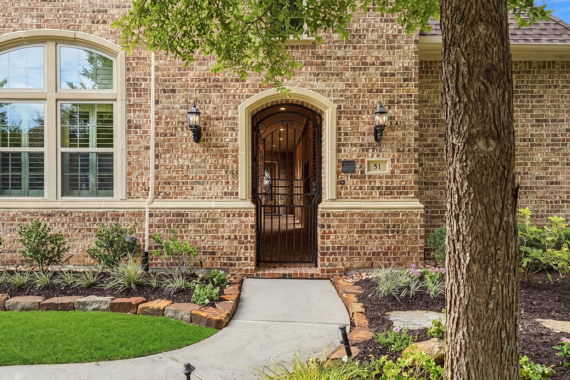 51 Woodglade Way, The Woodlands, TX 77375 A wrought-iron gate opens to a charming brick-lined entry, leading past the private guest casita and courtyard before arriving at the main residence.
