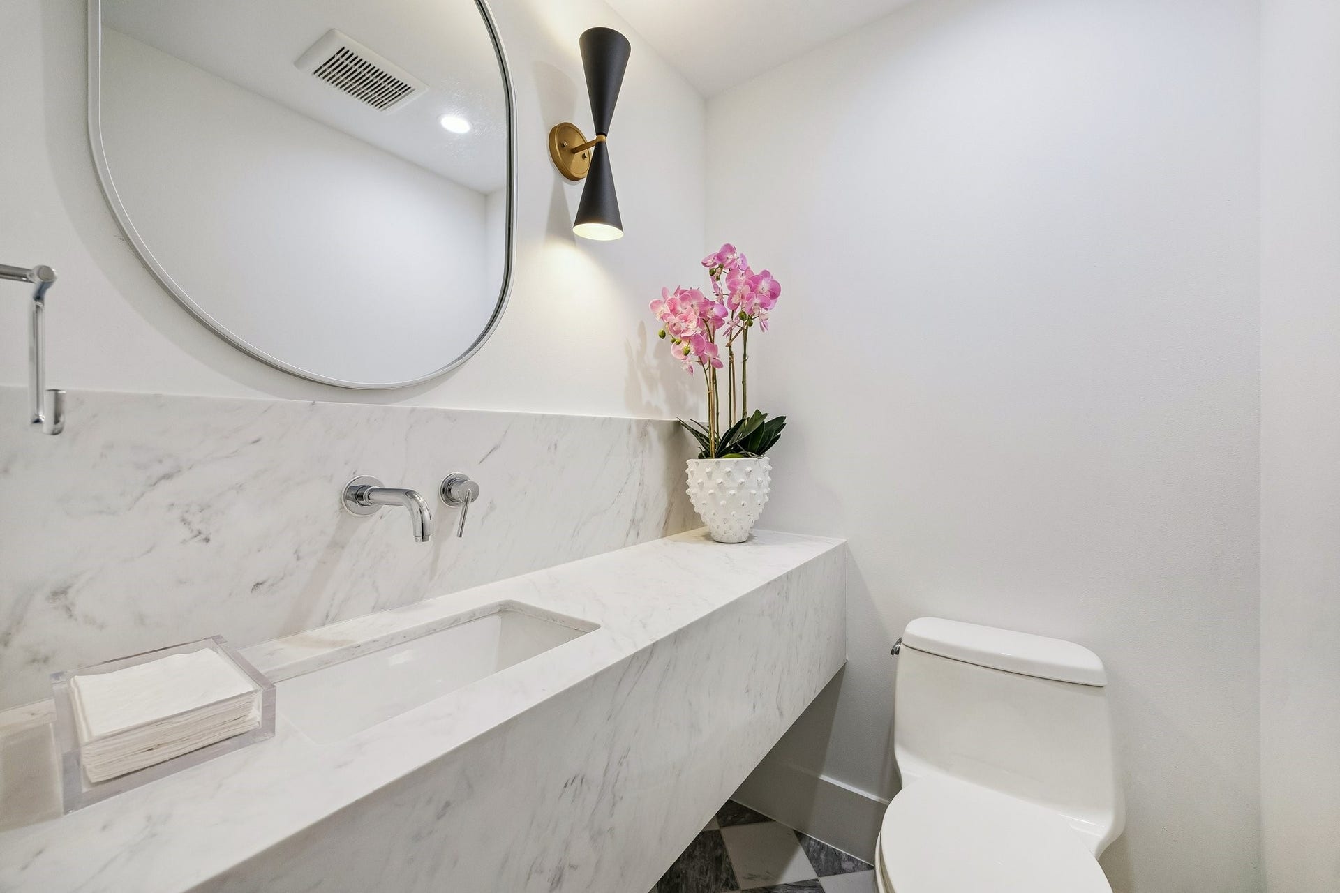 Second Powder Room located next to MUD Area to service the Back Covered Lanai with a 24 x 24 Checkerboard Matte Porcelain Tile in Calcutta and Amani Grey. Floating Slab Quartz Counter and Backsplash, Rectangular Undermount Sink, Wall Mounted Faucet in Polished Chrome, Oval Mirror and a Black/Gold Striped Sconce.