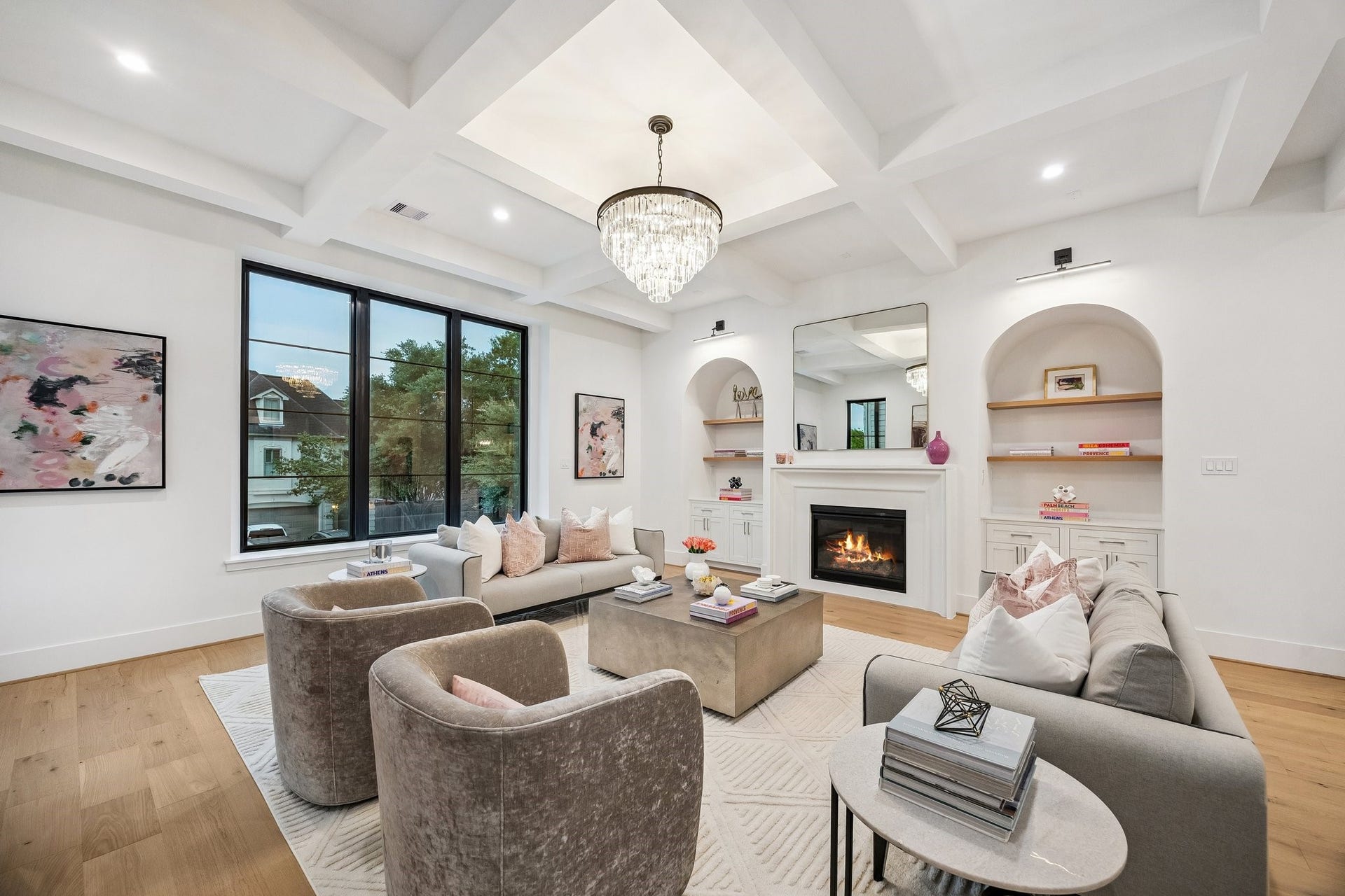 A refined yet welcoming living room that blends classic architectural details with modern comfort. Painted Boxed Beamed ceiling, Arched built-ins and a centered cast stone fireplace provide timeless structure, while soft lighting add warmth and sofistication. Large windows flood the space with natural light, making it ideal for both relaxing and entertaining.