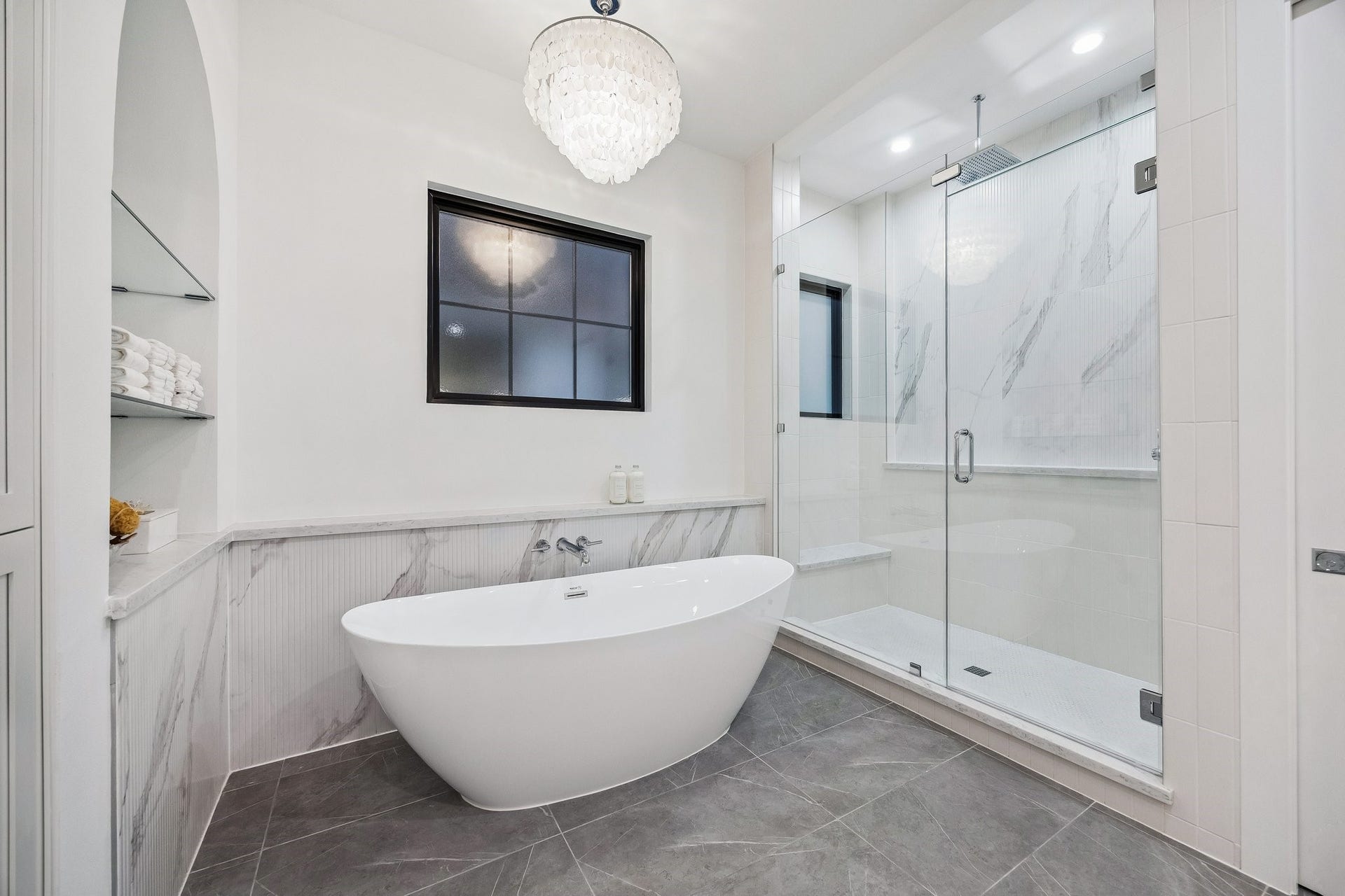 Large Walk-in Shower with a Framless Shower Enclosure. The Floor in the shower is adorned with White Matt Penny Round 2 x 2 Mosaic Tile. The Shower walls are a mixture 3 x 12 Vertical Matt Tile and 16 x 48 Ribbed Urbanslat Marmi Grey Tile.