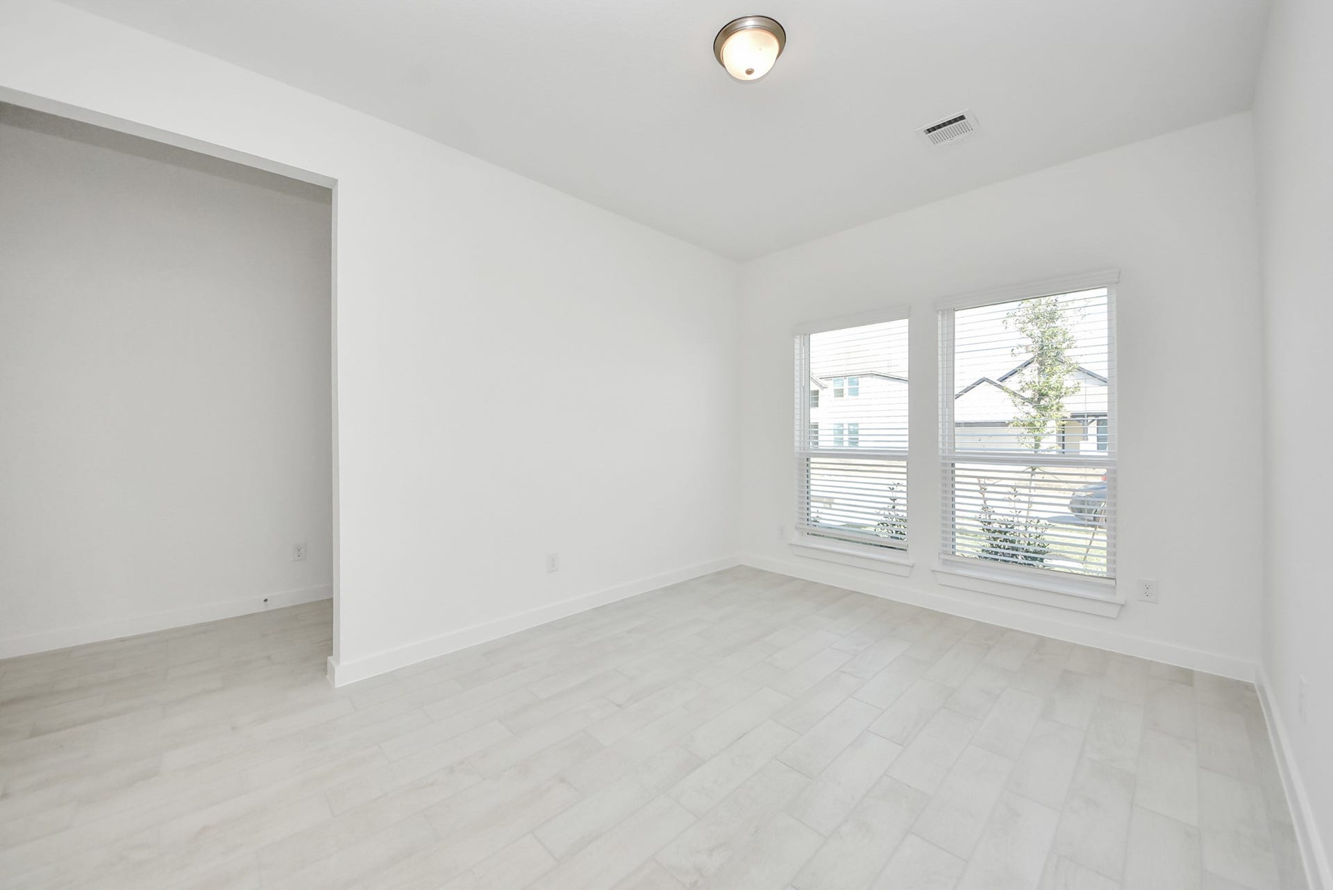 Experience the perfect blend of sophistication and warmth in this home office, boasting elegant wood-look tile flooring and flooded with natural light from expansive windows and French doors.