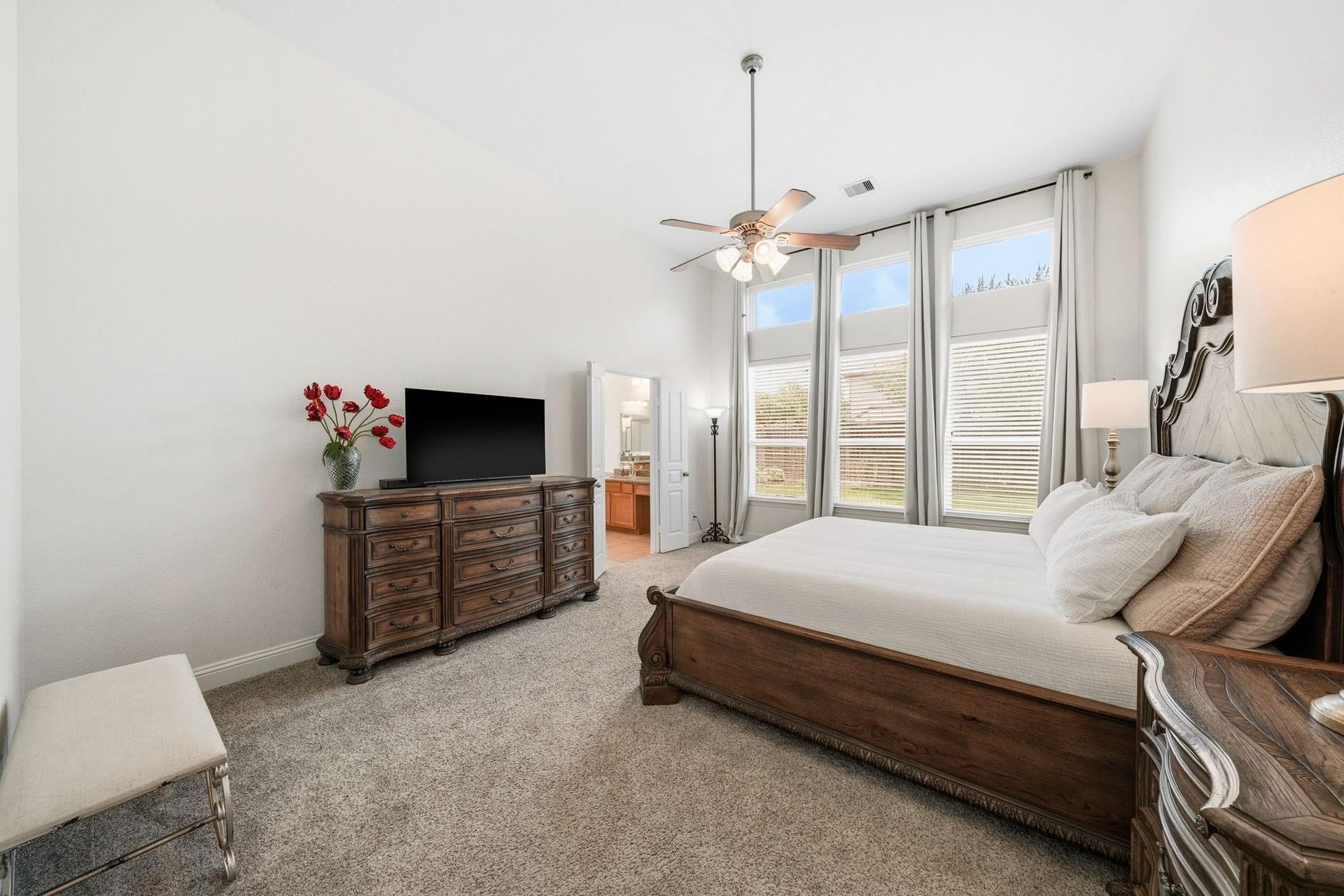 17610 Strackfield Lane, Tomball, TX 77377 Windows with elegant drapes stretch toward the ceiling, filling this primary bedroom space with sunlight and showcasing beautiful outdoor views.