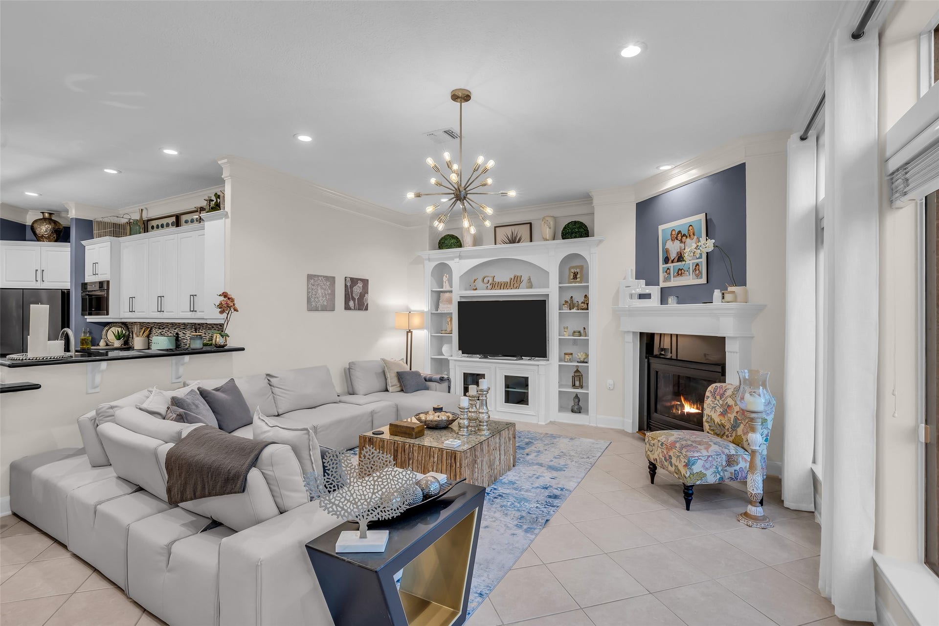 19023 Windsor Lakes Drive, Houston, TX 77094 Spacious living room with a cozy fireplace, elegant built-in shelving, and a modern light fixture. The open layout flows seamlessly into a stylish kitchen, perfect for entertaining.
