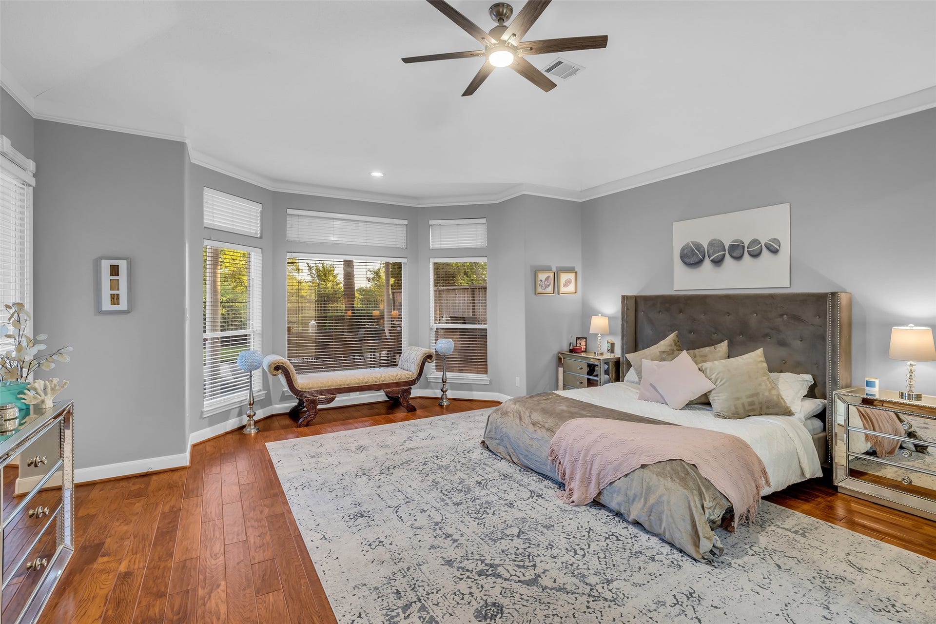 19023 Windsor Lakes Drive, Houston, TX 77094 Spacious primary bedroom featuring elegant wood floors, a cozy seating area by large bay windows, and a stylish ceiling fan, creating a serene retreat.