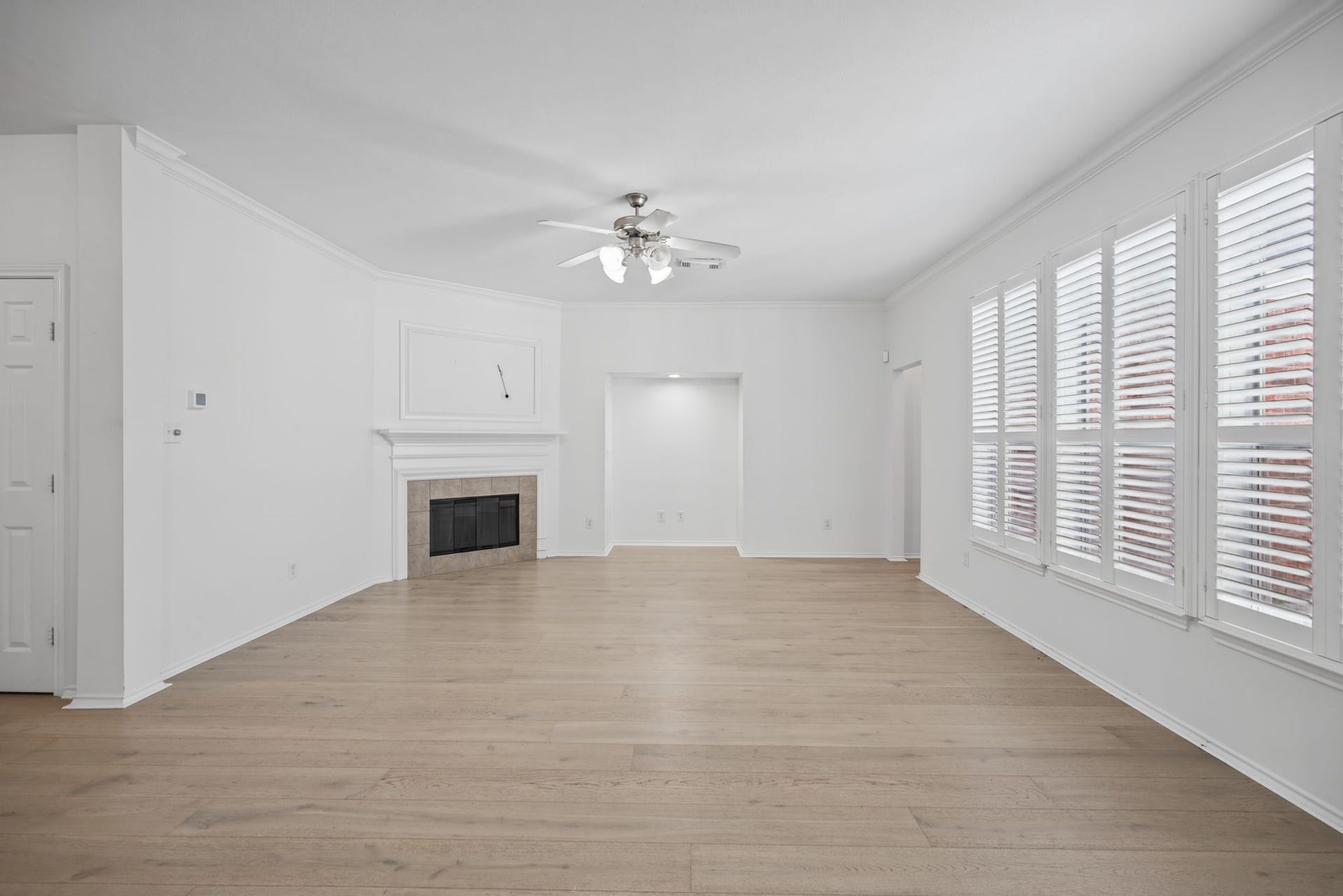 The main living room welcomes you with a fireplace framed by a white mantel, a ceiling fan, and an expansive row of windows.