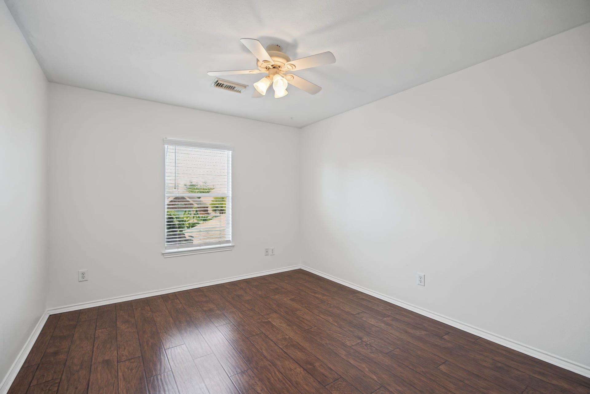 Continue to another bedroom, where dark-toned flooring, natural light, and a ceiling fan create a warm, restful setting.