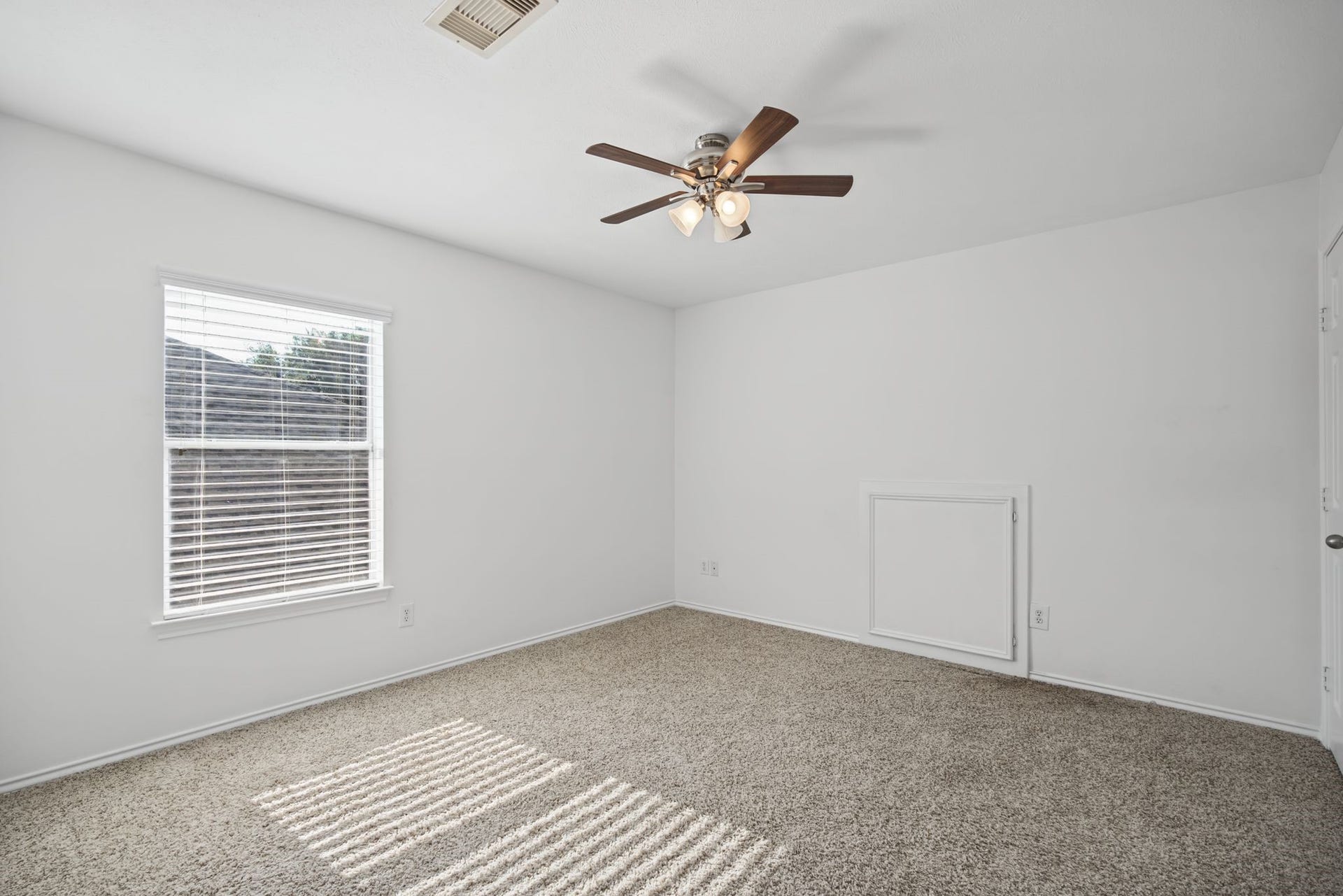 A secondary bedroom features soft carpeting and sunlight filtering through window blinds, with a ceiling fan overhead.