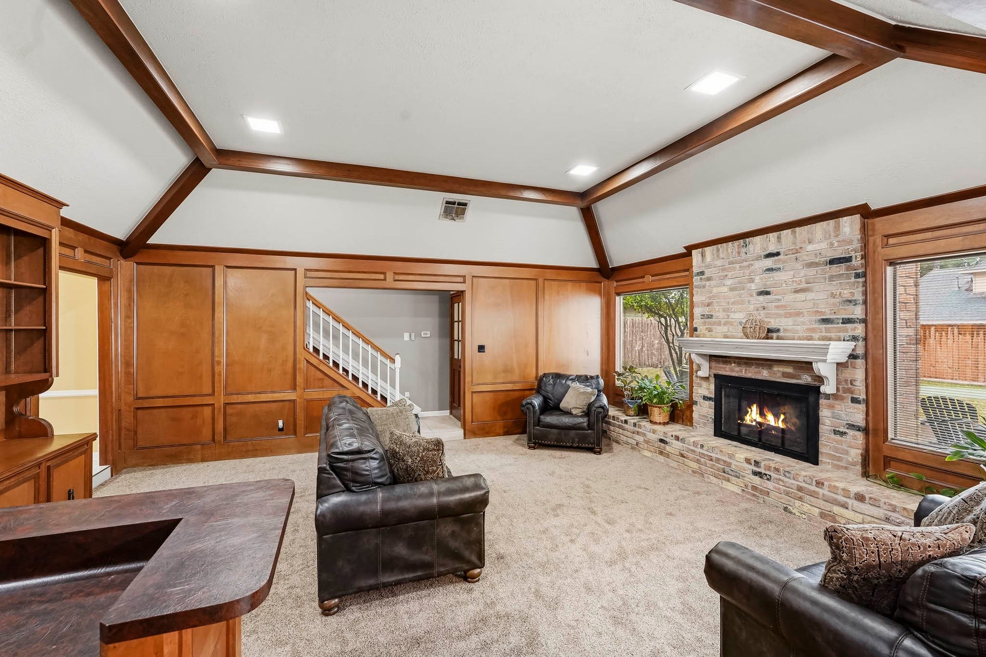 3610 Valley Haven Drive, Houston, TX 77339 Spacious living room featuring rich wooden paneling and beams, a cozy brick fireplace, and plush carpeting, creating a warm and inviting atmosphere.