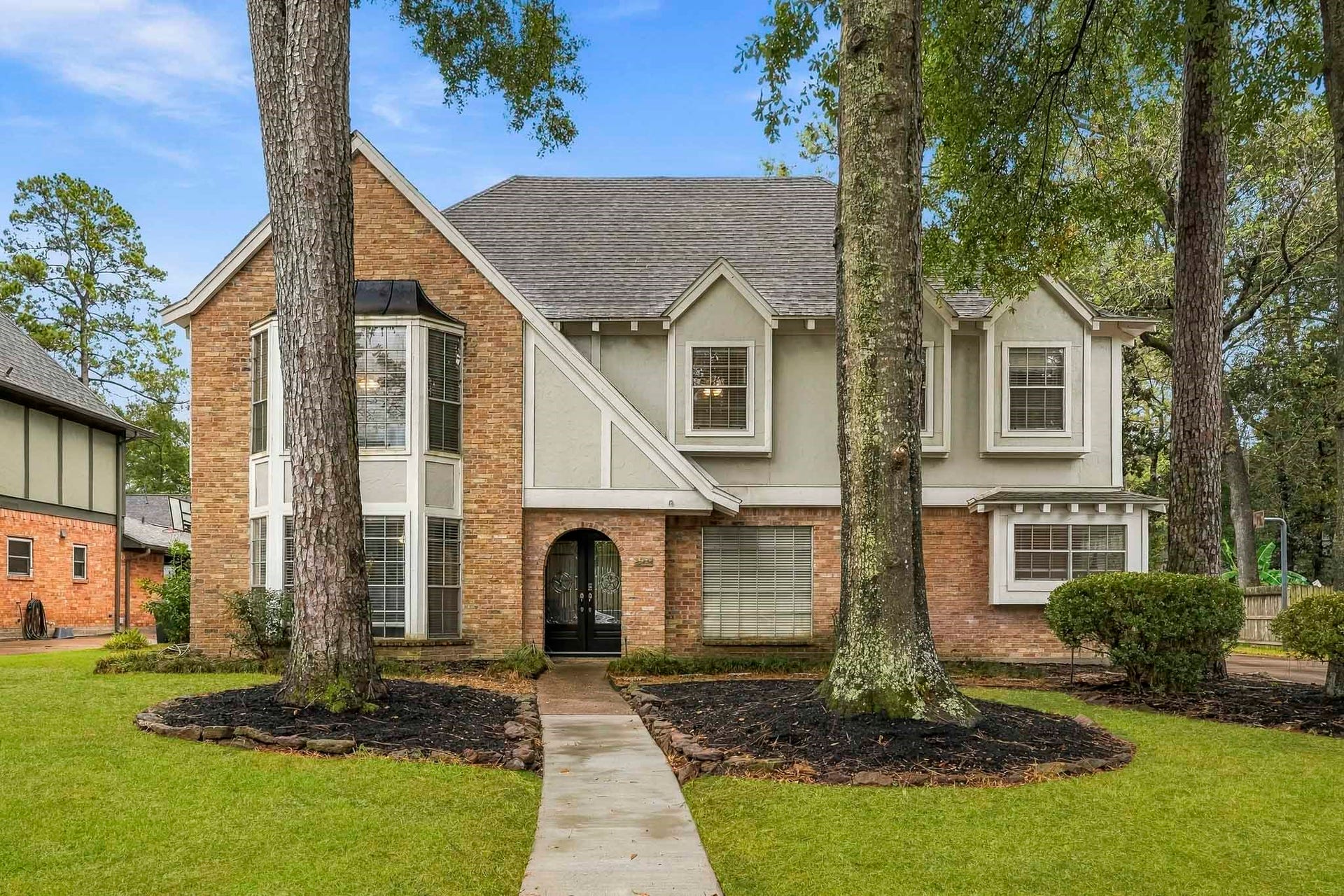 3610 Valley Haven Drive, Houston, TX 77339 Charming two-story home with a classic brick and stucco exterior, featuring a welcoming archway entrance and large bay windows. Nestled among mature trees, this property boasts a well-manicured lawn and a serene suburban setting.