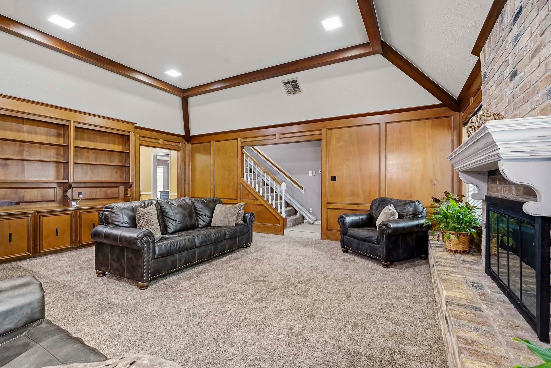 3610 Valley Haven Drive, Houston, TX 77339 Spacious living room featuring elegant wood paneling, a cozy fireplace with a brick surround, built-in shelving.