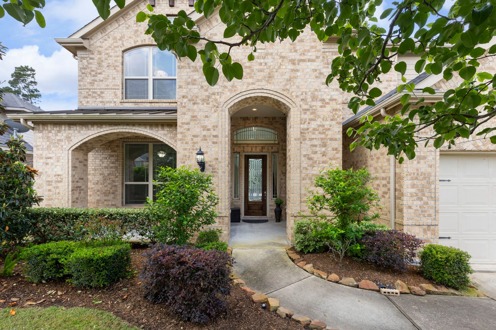 10235 S Goshawk Trail, Conroe, TX 77385 Inviting front entry with arched brick detailing and landscaped walkway leading to a covered porch.