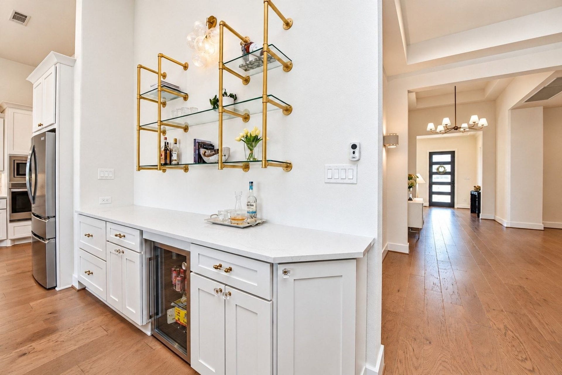 20222 Palomar Pointe Drive, Cypress, TX 77433 Custom open shelving unit with gold accents features a built-in beverage refrigerator. The adjoining area flows seamlessly into a bright hallway with stylish lighting and wood flooring.