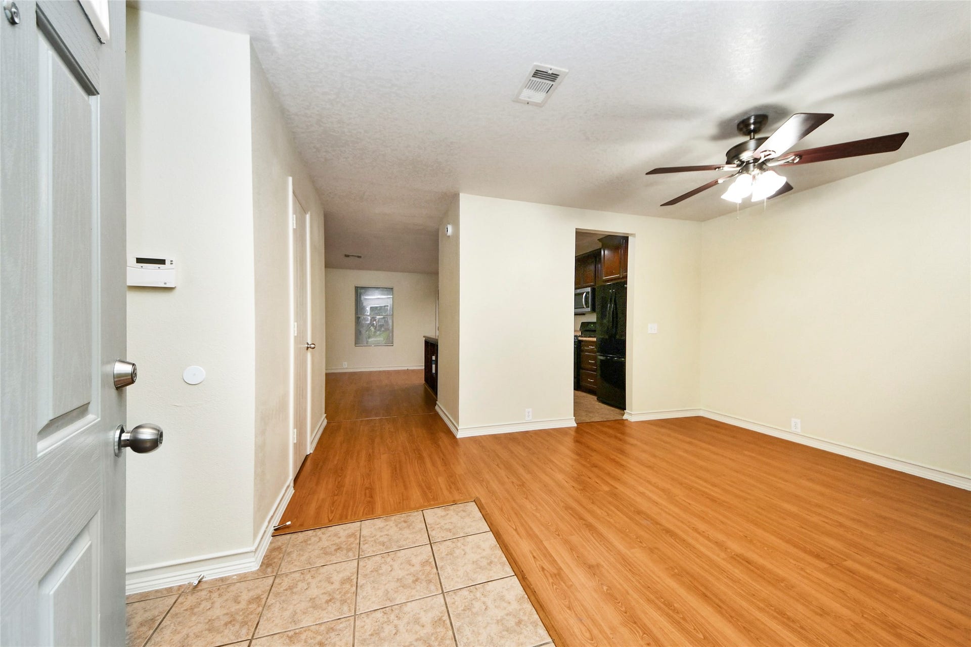 Step into a welcoming den with warm wood flooring, seamlessly leading to the kitchen, perfect for relaxation and entertaining.