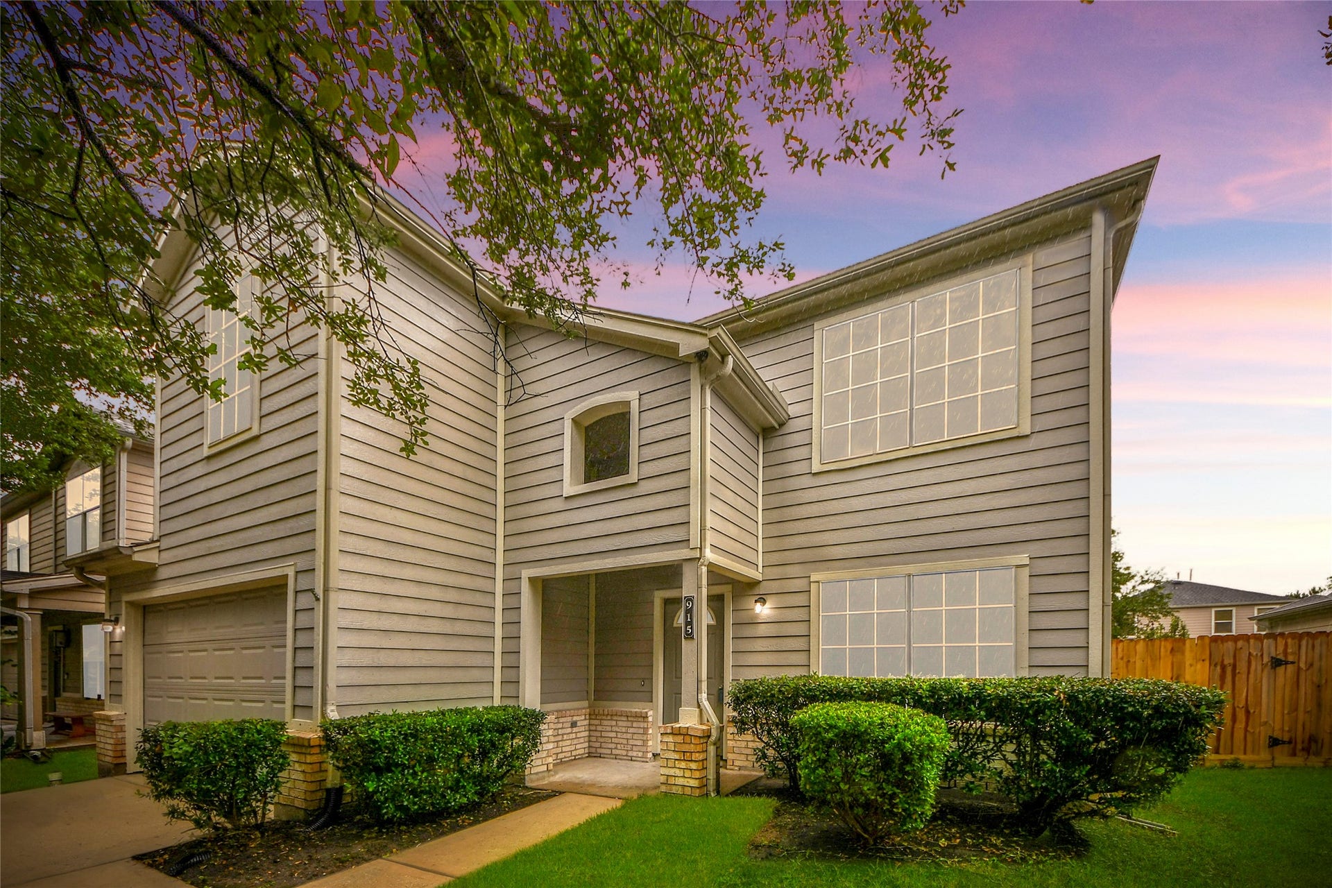 Charming two-story home with a welcoming front entrance and attached garage, set against a picturesque sunset sky.